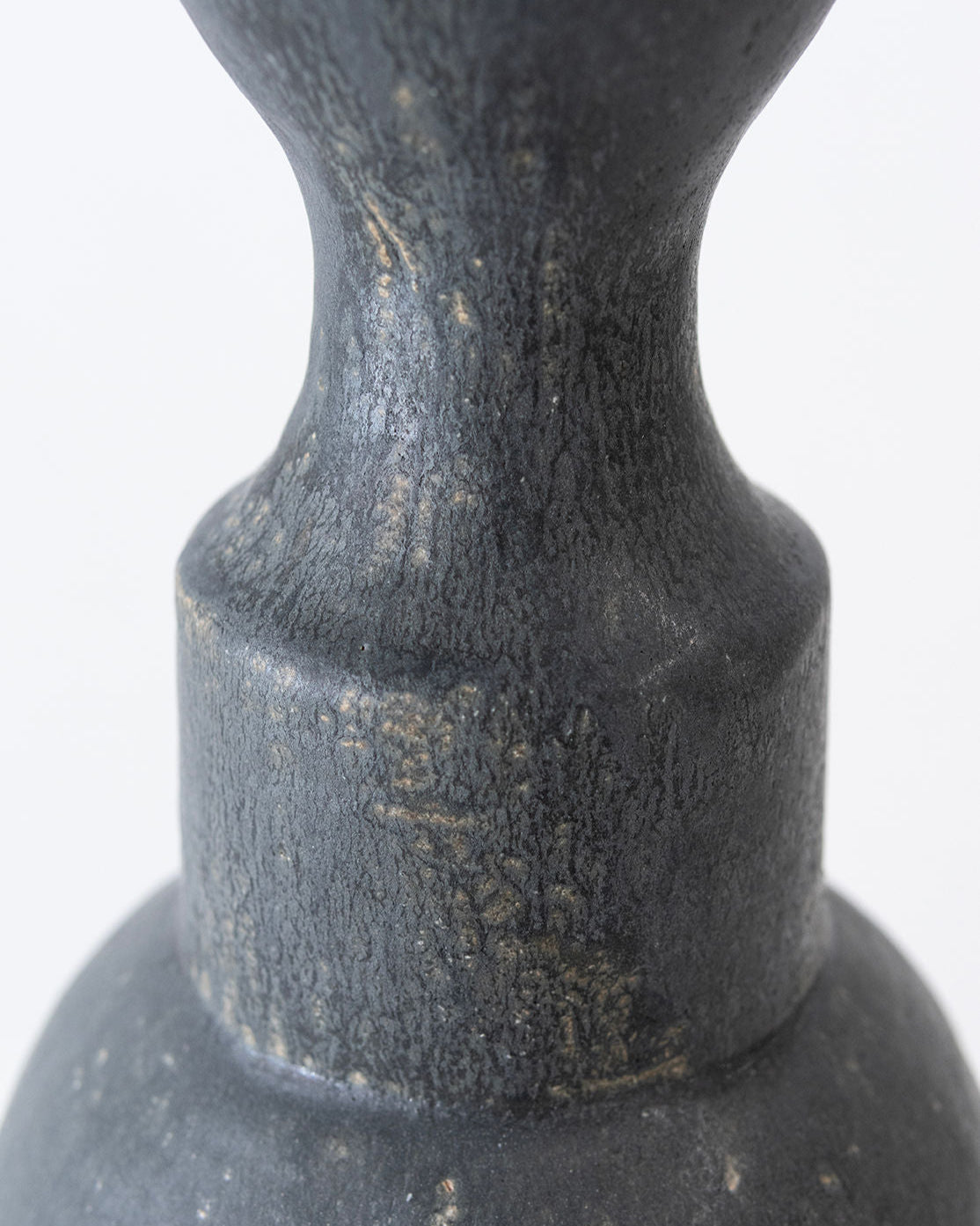 Close-up of the 'Isolated n.36' Vase by Canoa Lab, featuring a textured dark gray surface, rounded and slightly tapered neck, and matte finish. The background is softly blurred with a light tone.