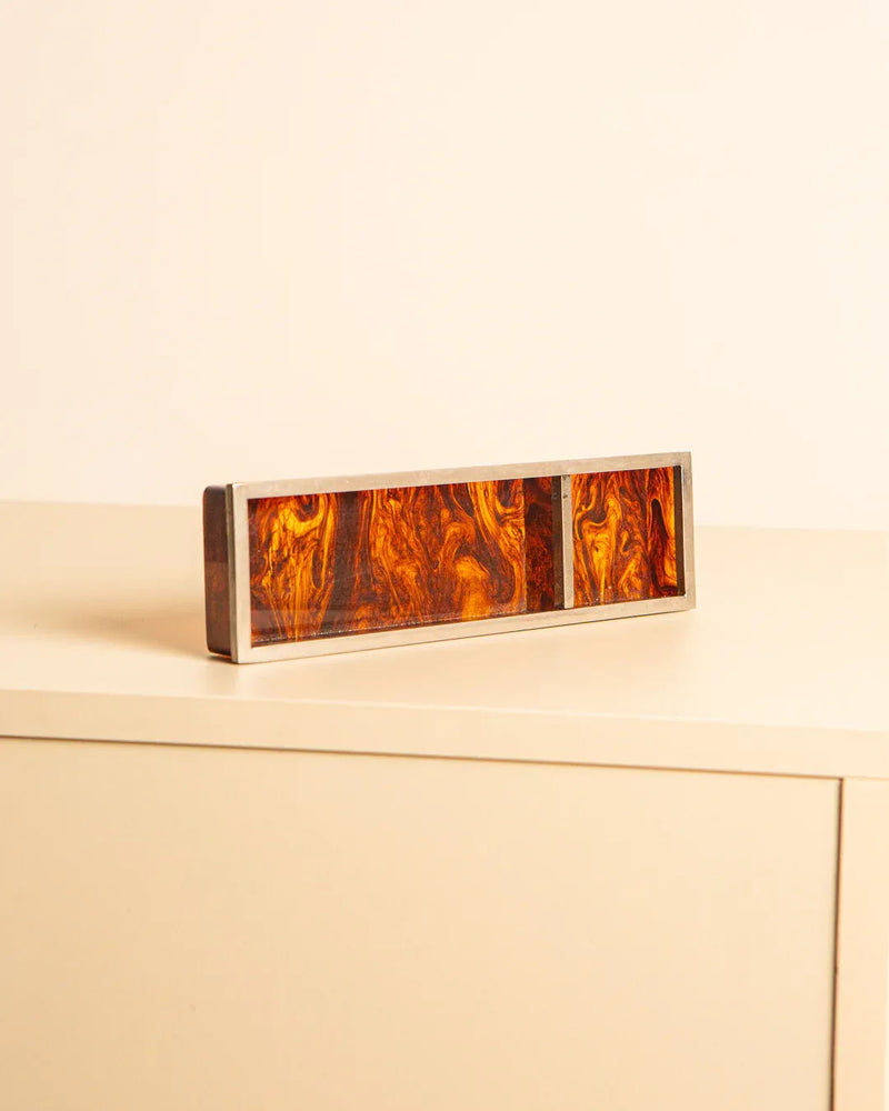The Vide Poches Italian 80s panel by Treaptyque displays an abstract, tortoiseshell wood texture in brown and amber, set against a light surface with a beige backdrop. This rectangular piece boasts metallic edges inspired by elegant Italian design.