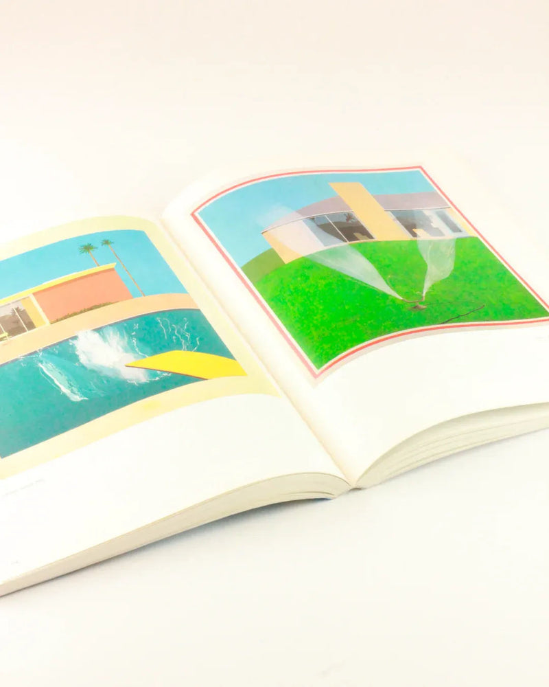 An open David Hockney 'My Early Years' from Boga Avante Shop features colorful illustrations reminiscent of David Hockney. The left page shows a diving board above a swimming pool in front of a modern house with palm trees, evoking the essence of arte británico. The right page depicts a green lawn with a sprinkler watering the grass next to another modern house.
