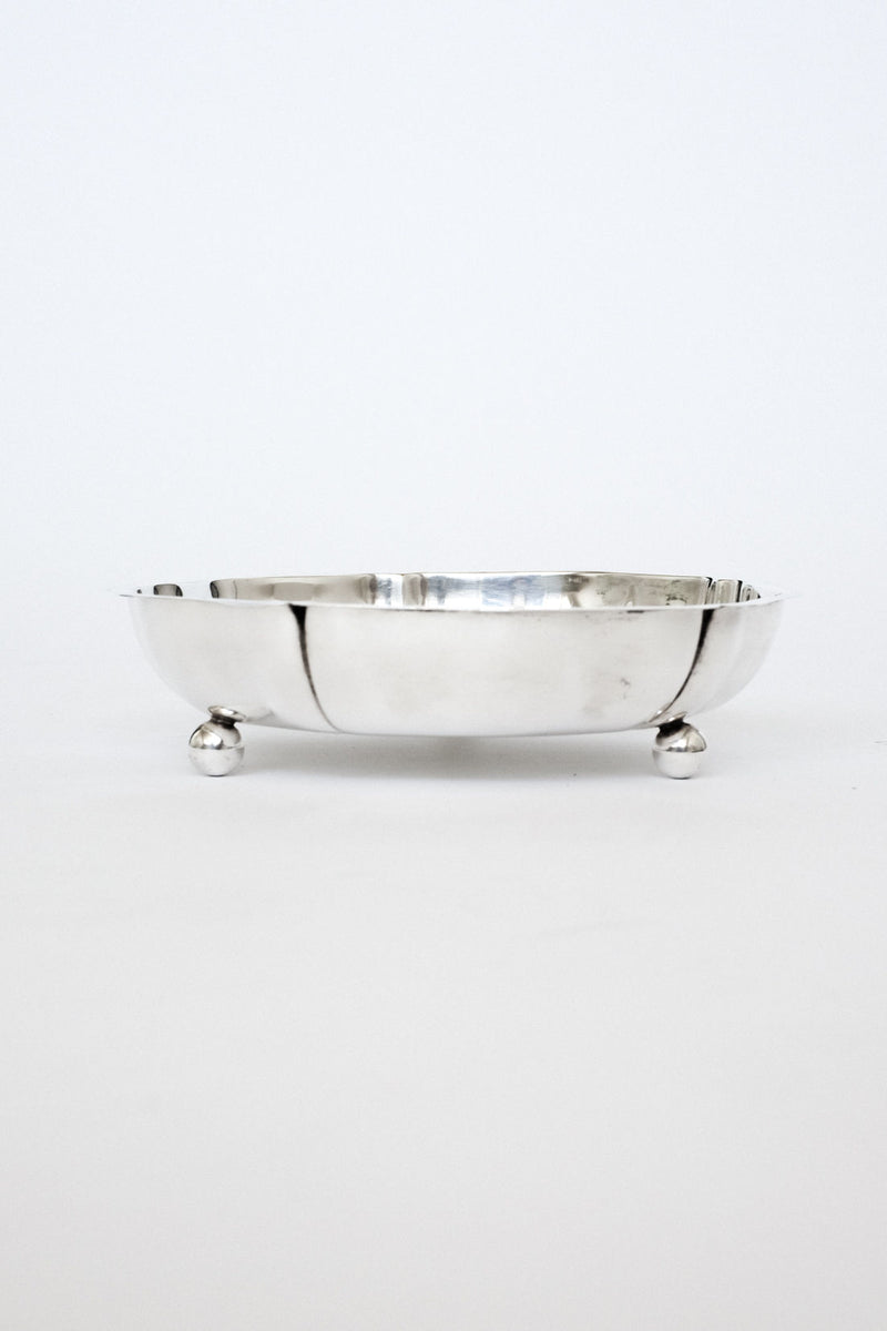 The Silver-plated Bowl by septembre studios features a smooth, round design with three ball-shaped feet, displayed on a plain white background, highlighting its vintage serving dish charm.