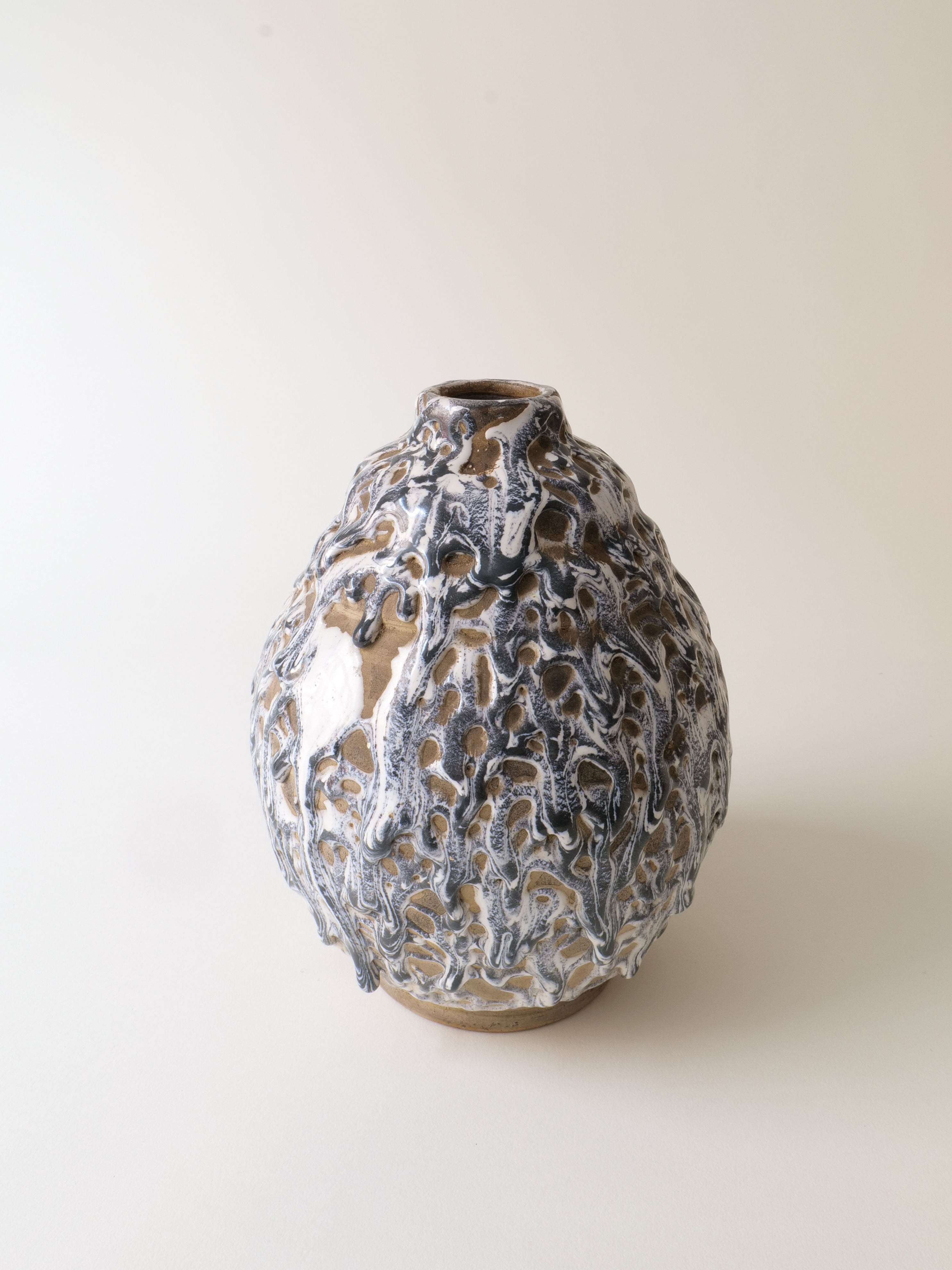 The Deco Ceramic Vase 1930s by Collection apart features a round stoneware design with an uneven, textured surface in black, white, and beige colors on a plain white background. Its unique organic look evokes the artistic style of Alfred Renoleau.