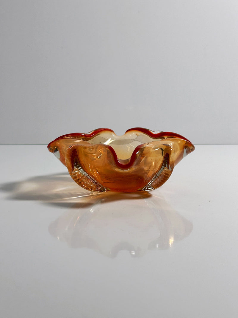 A Venetian Ashtray by Seguso Murano from the 1950s, offered by Dodo Vintage, sits on a flat white surface. Light reflects beneath its wavy-edged glass bowl with coral hues, enhancing its warm colors and fluid nautical design.