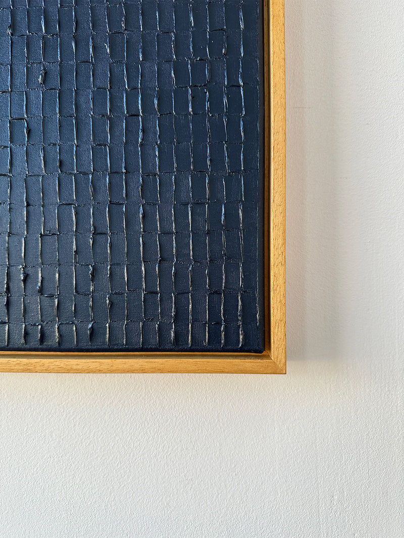 The "Prussian Blue - Oil on canvas" by Roi Elmaliah, ready to ship from Amsterdam, showcases a textured black pattern with a grid-like design. It is elegantly framed in light wood, mounted on a plain white wall that highlights its dark background beautifully.