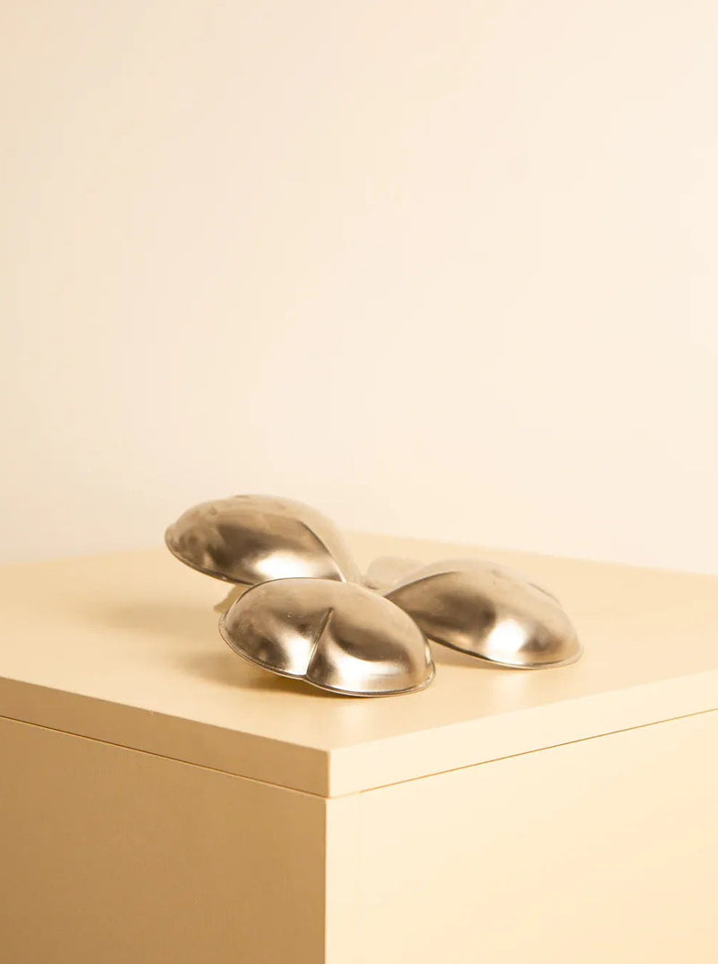 A sleek, modern abstract sculpture with interlocking metallic shapes, reminiscent of '80s design, rests on a minimalist light-colored pedestal against a plain background. The stainless steel surfaces are smooth and reflective, lending a contemporary aesthetic to the piece that echoes Treaptyque "Trefoil" shaped vide-poches 80's design.