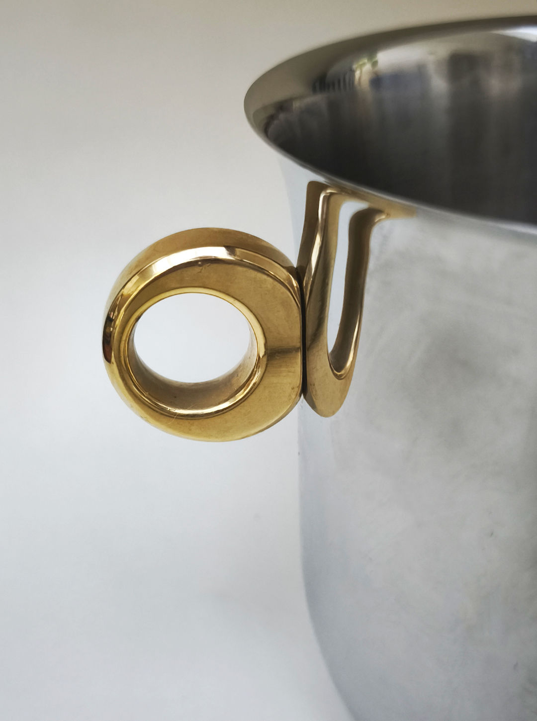 Close-up of the Les Objoies "Ice Bucket, Italy 1970s," crafted in stainless steel with a shiny gold brass ring handle on its side, set against a neutral background.