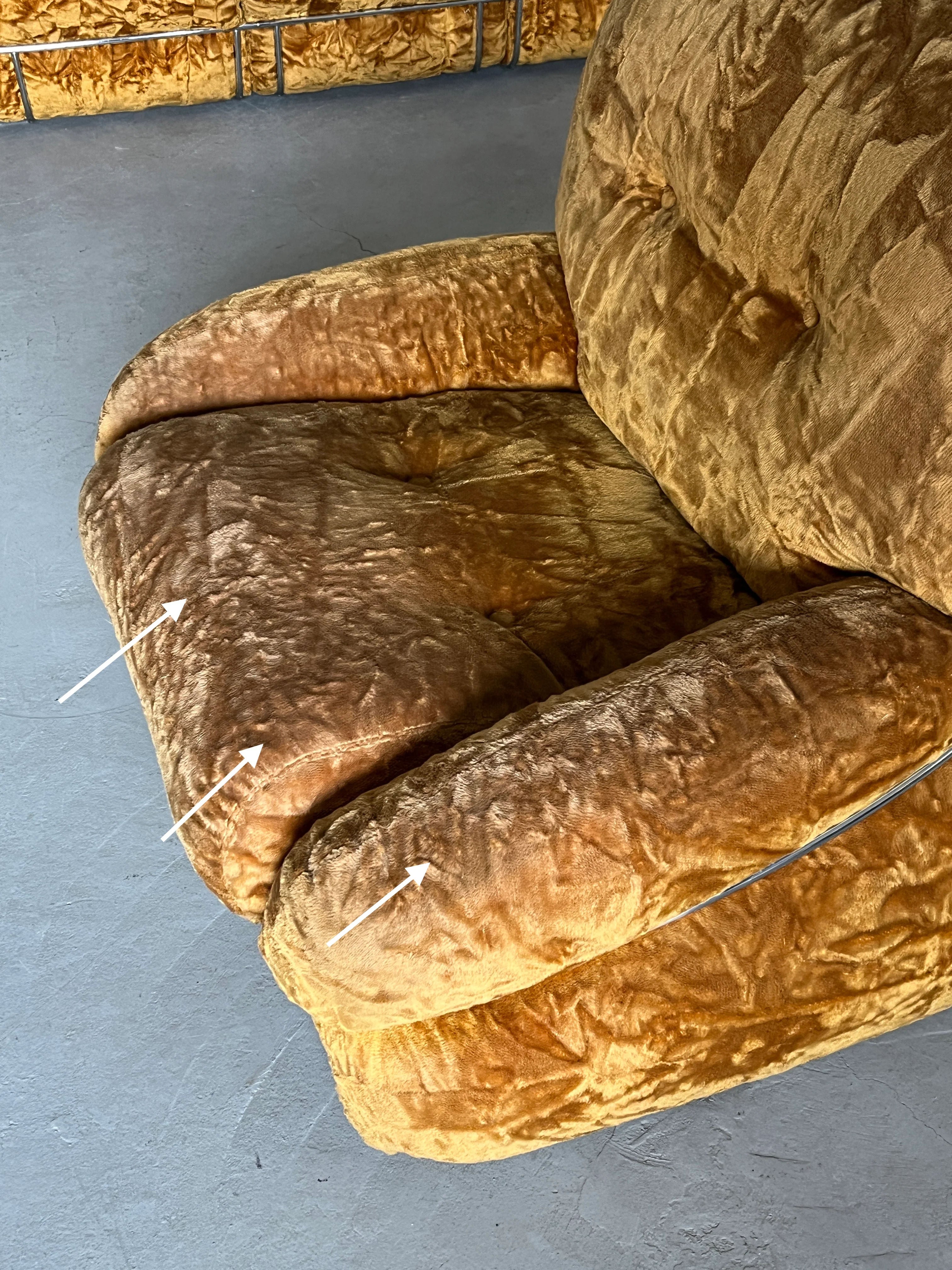 A close-up of an aged, brown recliner crafted from ochre velvet shows visible wear. The fabric appears faded and creased with arrows pointing to worn areas on the seat and armrest—an iconic Mid-Century piece resembling Cherry Cargo's Adriano Piazzesi 'Okay' Sofa Seating Set from the 1970s.