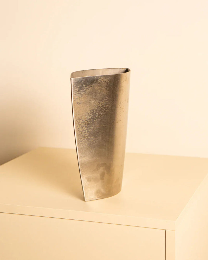 Treaptyque's 80's Italian Metal Vase, tall and rectangular with a slight curve, highlights its craftsmanship on a light-colored minimalist cabinet against a warm beige wall.