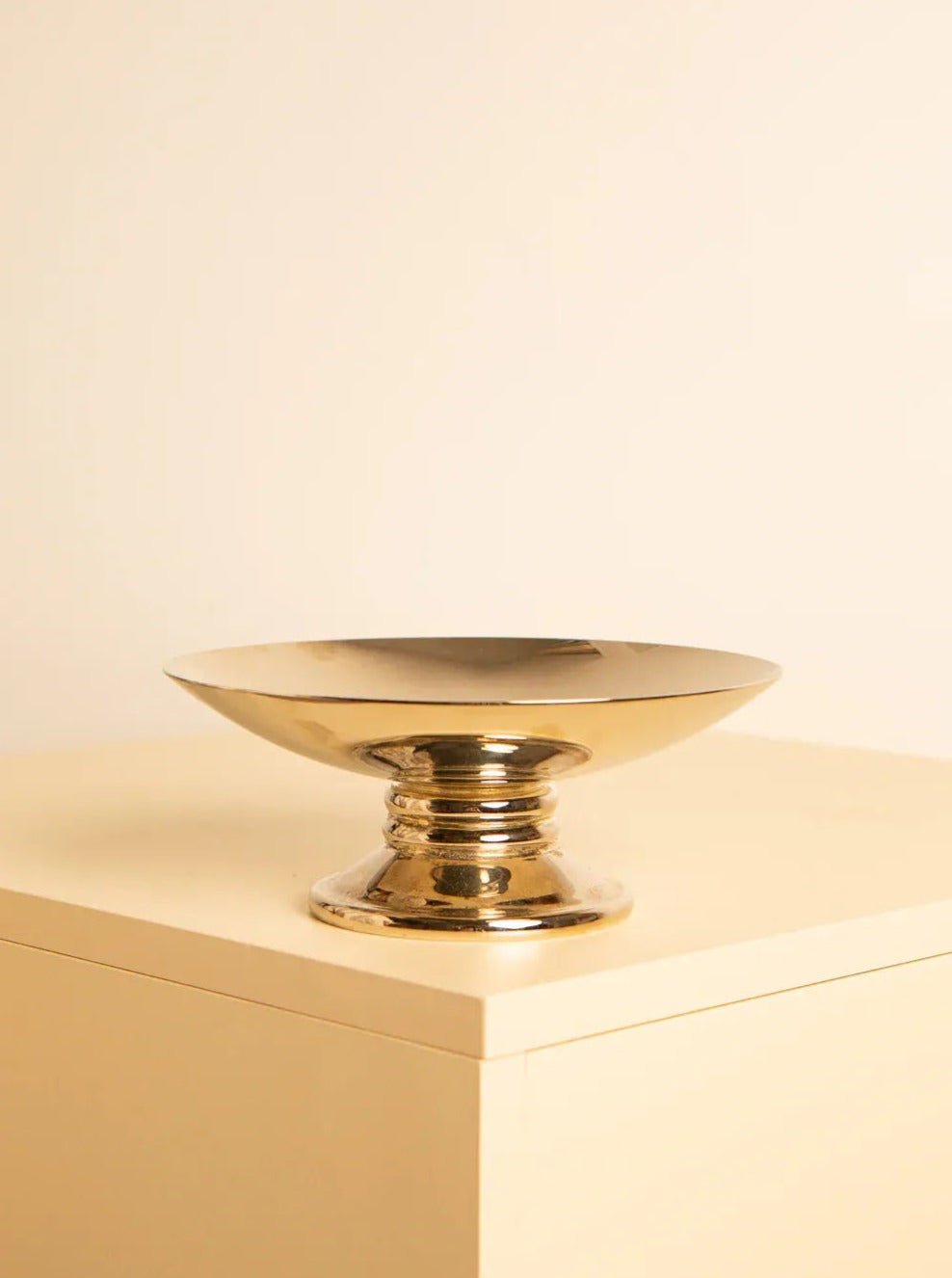 A polished 80's Silver Plated Bowl from Treaptyque with a wide rim and a sturdy pedestal base sits on a light beige tabletop against a matching beige background. The setting creates a warm, minimalistic aesthetic, highlighting the bowl's impeccable condition.