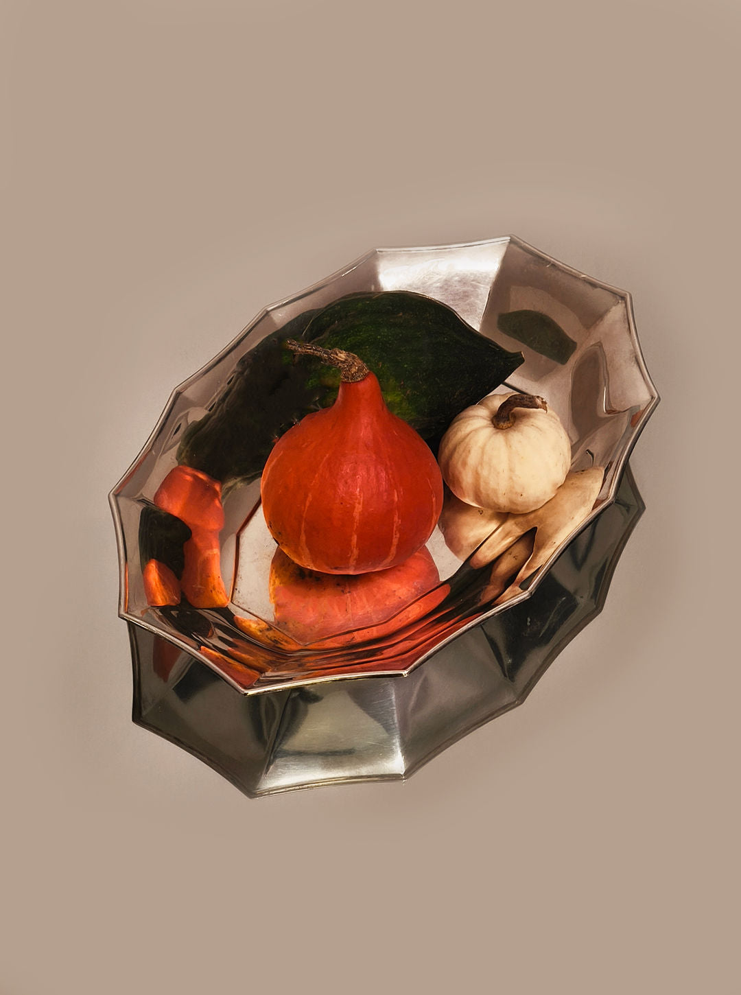 A reflective Les Objoies silver-plated tray displays assorted vegetables: a small orange pumpkin, white gourd, dark green squash, and carrots. The tray's sophisticated mirrored surface enhances the colorful arrangement.