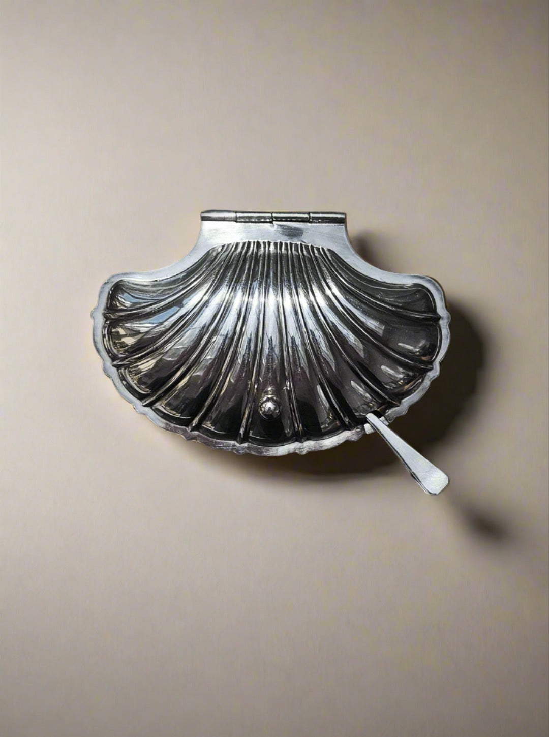 A Shell Silver-Plated Butter Dish by Les Objoies in a charming seashell shape features a latch on the top and is displayed against a plain background. The container boasts a shiny, polished finish, with a small key or handle attached at the bottom, adding to its vintage charm.