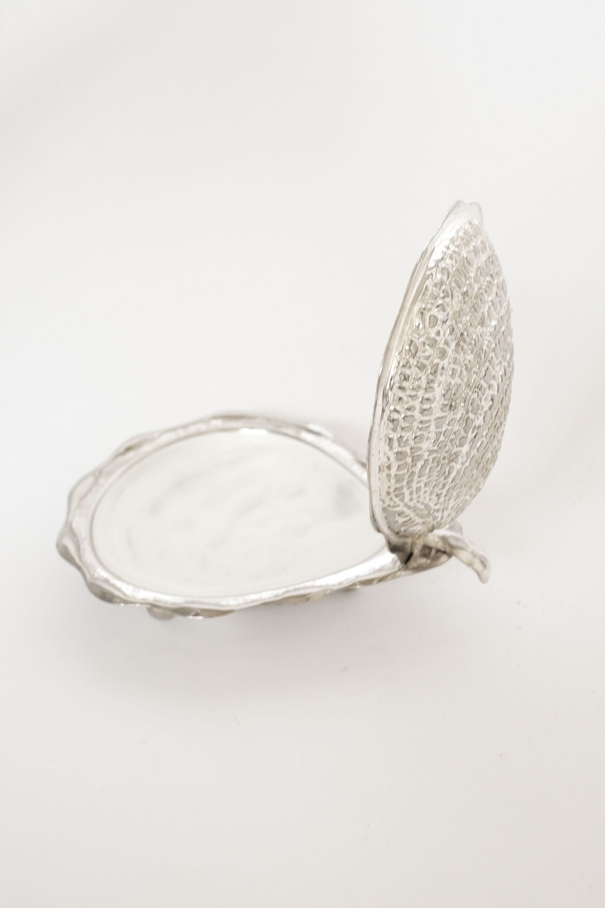 The septembre studios Shell Butter Dish features a vintage silver clam shell-inspired design with a hinged lid. Shown open against a plain white background, its smooth interior contrasts with the textured exterior.