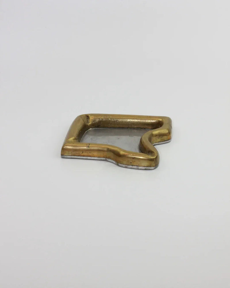 A vintage brass Brutalist Ashtray from Boga Avante Shop in the shape of a speech bubble lies on a plain white background. The ashtray, reminiscent of a Brutalist style, has acquired some patina over time, indicating it's been used or aged.
