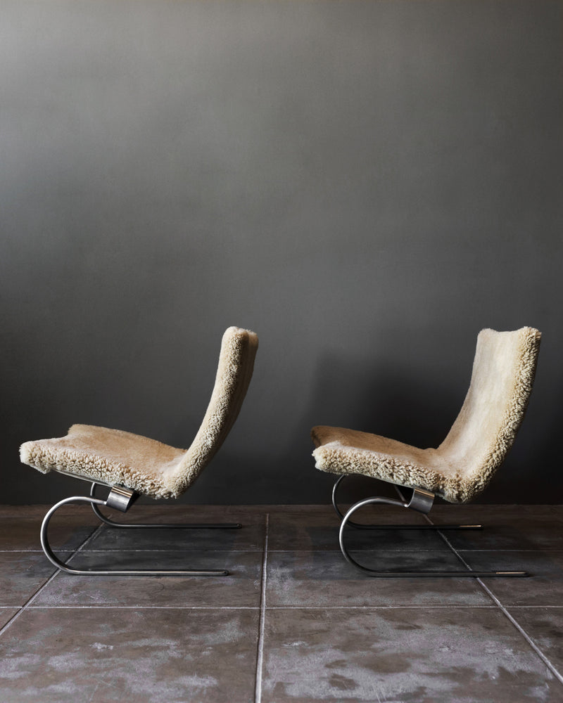 A pair of PK20 chairs by Poul Kjaerholm in shearling from Studio OSKLO, with sleek curved frames and cozy upholstery, sit side by side on a tiled floor against a plain dark gray wall.