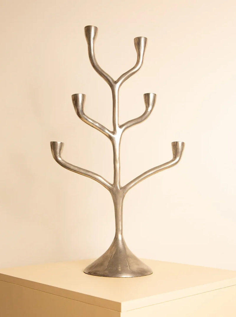 A sleek, modern silver candelabrum, known as the Italian Candleholder 80s by Treaptyque, is displayed atop a beige surface against a soft cream-colored background. Made from cast aluminum and showcasing impeccable Italian craftsmanship, its design resembles a minimalist tree with each branch holding a single candle holder.