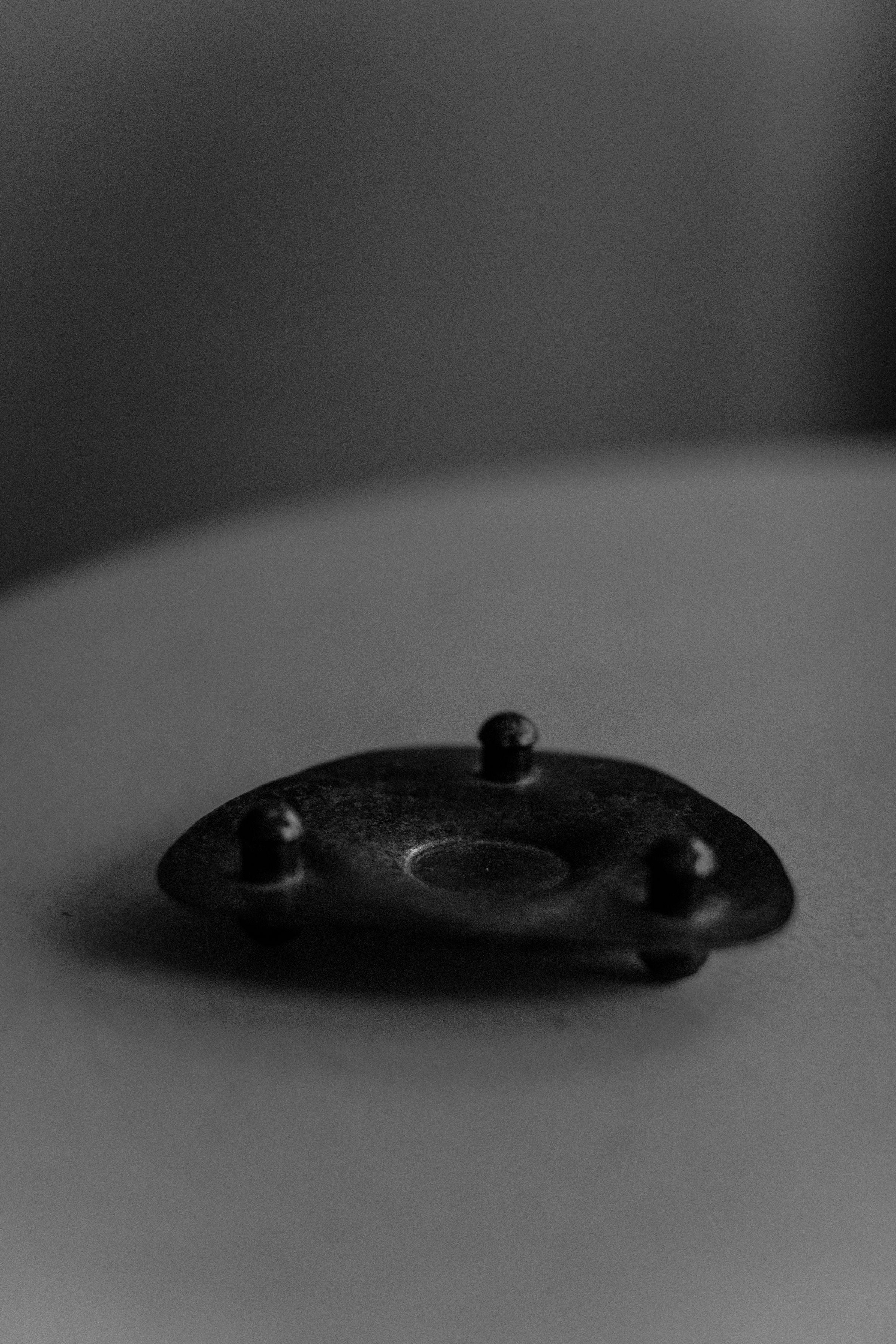 Close-up of an Out For Lunch Brutalist Candleholder with a circular center and four surrounding bolts on a soft-focus light gray surface, displaying a moody, dramatic aesthetic with a weathered finish.