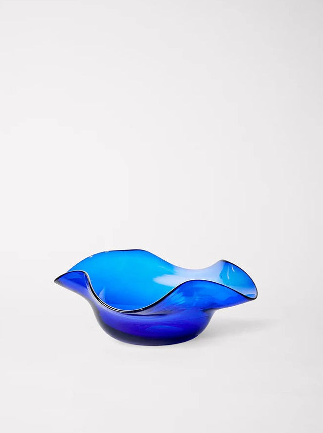 A vibrant blue Michele Bowl Small from Akua Objects is displayed against a plain white background. The handmade Venetian piece has a dynamic, wavy design with undulating edges, creating an artistic and fluid appearance. The smooth, reflective surface enhances its modern aesthetic.