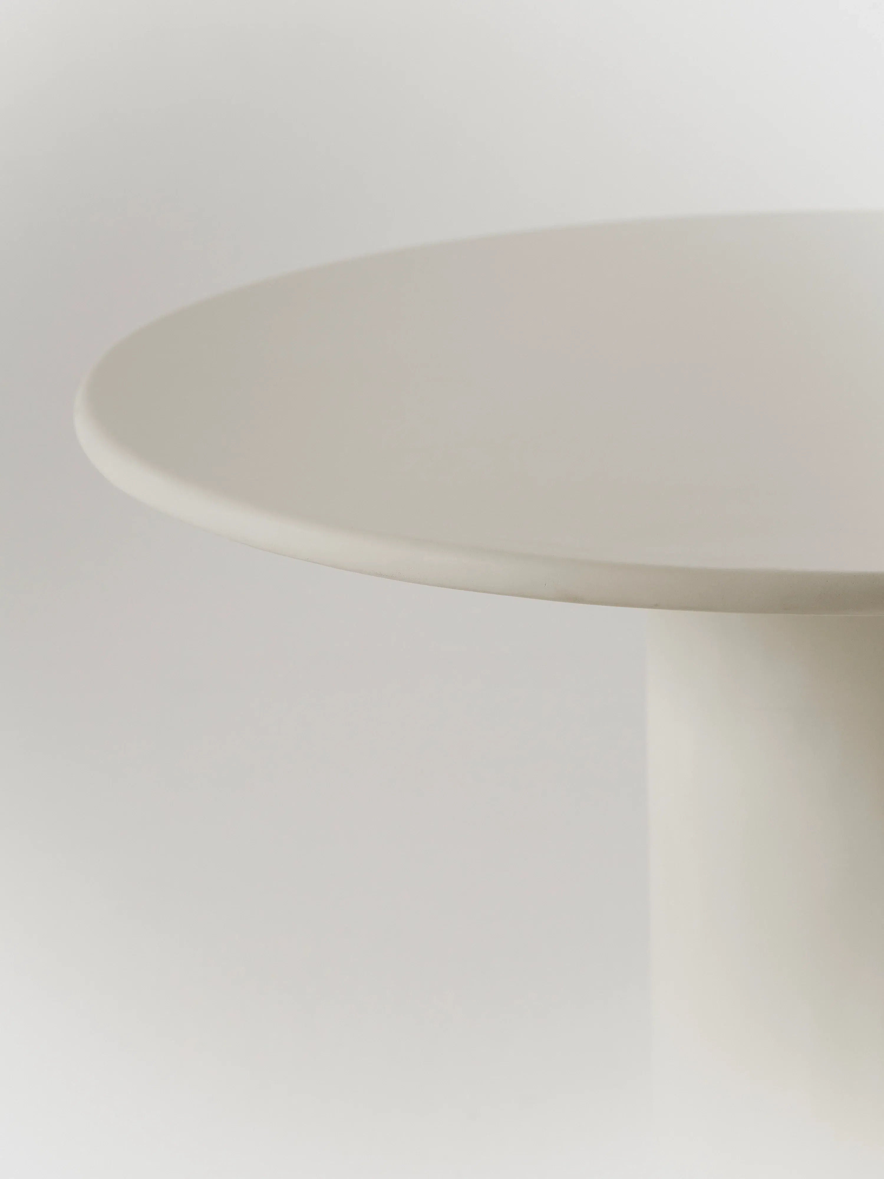 Close-up of the Gio Dining Table by MarlotBaus, featuring a round microcement top with a smooth finish. The image showcases its minimalist design and wooden legs against a light gray background.