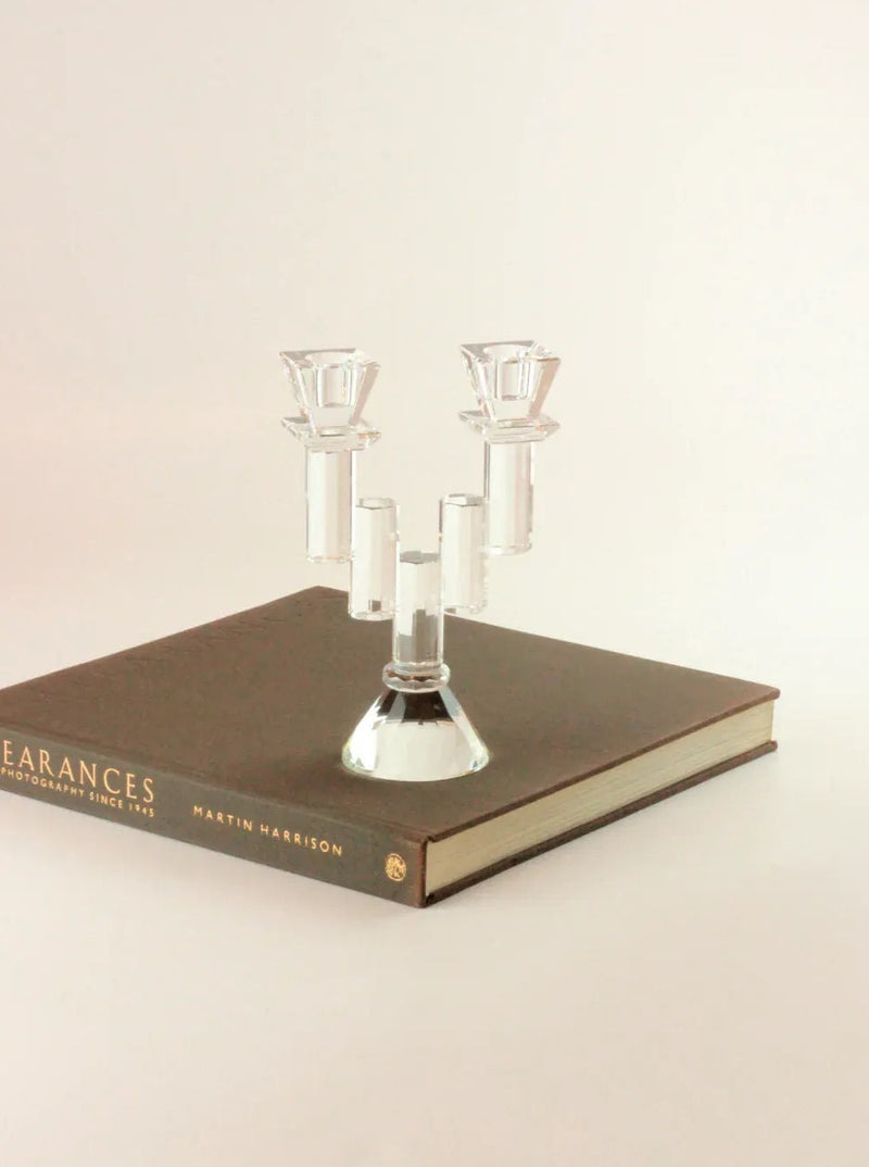 A Faceted Crystal Candleholder by Boga Avante Shop, evoking a vintage item, is placed on top of a closed hardcover book titled "Appearances: Photographs Since 1935" by Martin Harrison. The background is plain and light-colored, highlighting the simple and elegant setup.