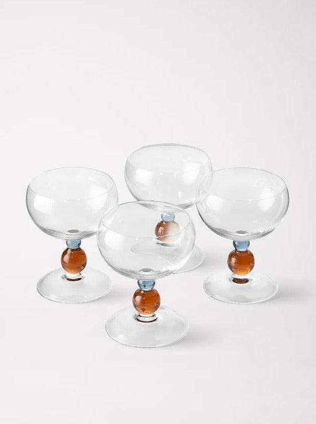 Four Noam Wine Glasses - Set of Four by Akua Objects with round brown bases, arranged in a cluster on a plain white background. The glasses have prominent round stems, each featuring a blue ring at the bottom. Perfect for festive table settings, they add an elegant touch to any celebration.