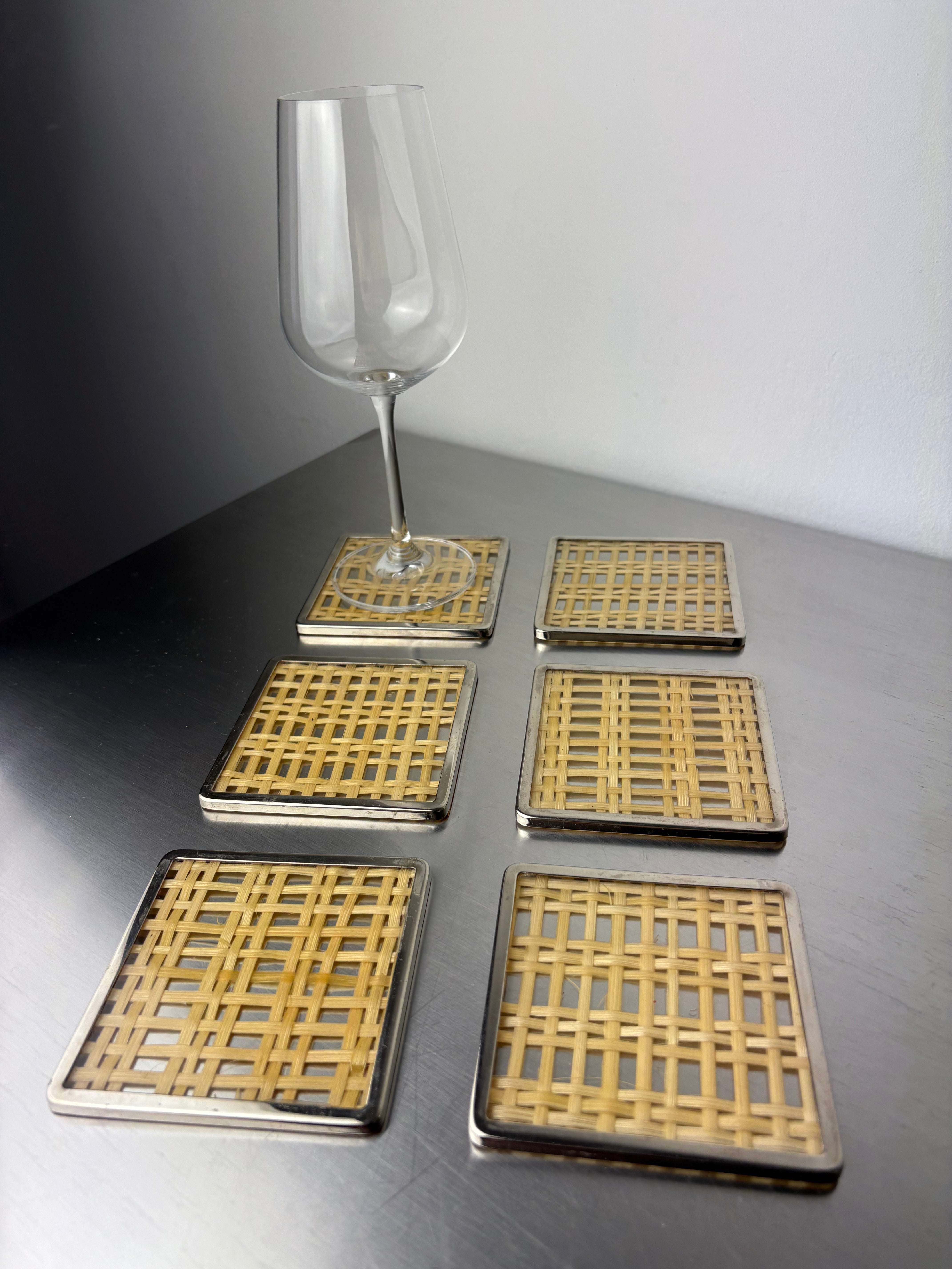 Six lucite rattan coasters arranged on dark surface with wine glass