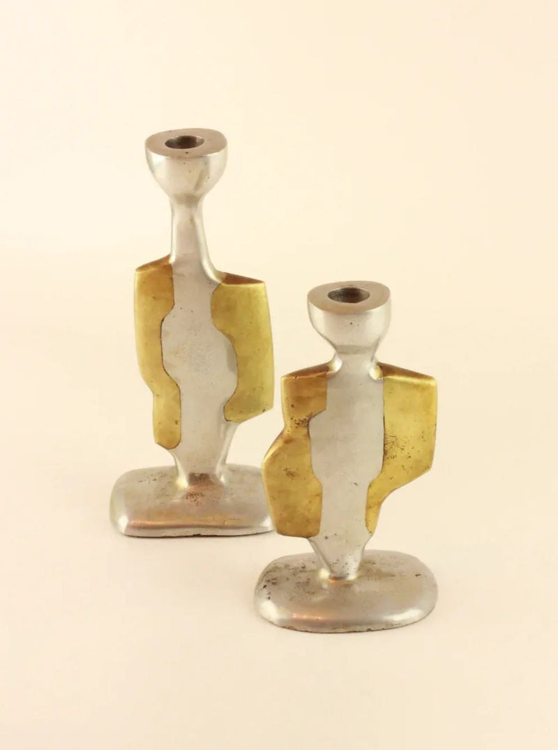 Two vintage Brutalist Candleholders made of a combination of aluminum and brass from Boga Avante Shop. Each holder has a unique, abstract design featuring geometric shapes and a sturdy base. They are positioned side by side on a plain background, with one slightly in front of the other.
