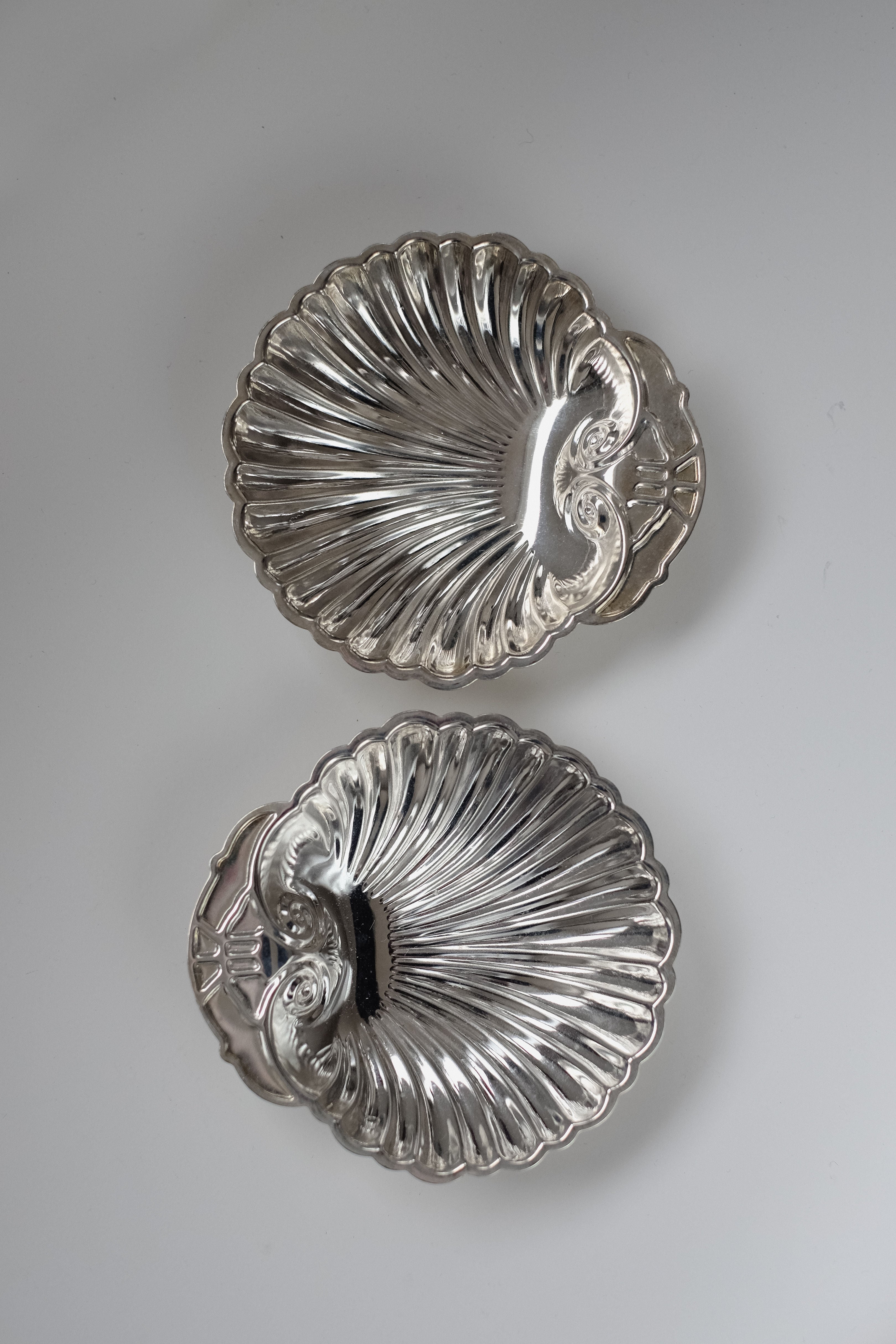 A Set of 2 Silver-plated Shell Trays by septembre studios lies on a flat surface, showcasing ribbed patterns and intricate detailing, perfect for enhancing elegance during any dining experience.