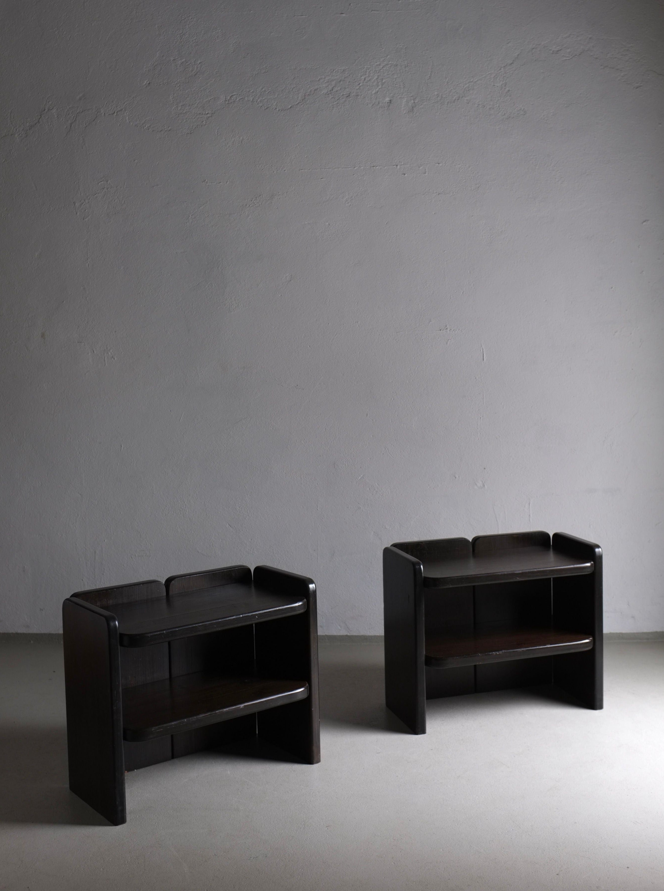 Two Veter Vintage 2 Brutalist Dark Wood Night Stands | 1970s, in vintage condition, are placed against a plain, light gray wall. The night stands have a simple, modern design with curved edges and a minimalist aesthetic. The room appears empty with a smooth floor, emphasizing the furniture.