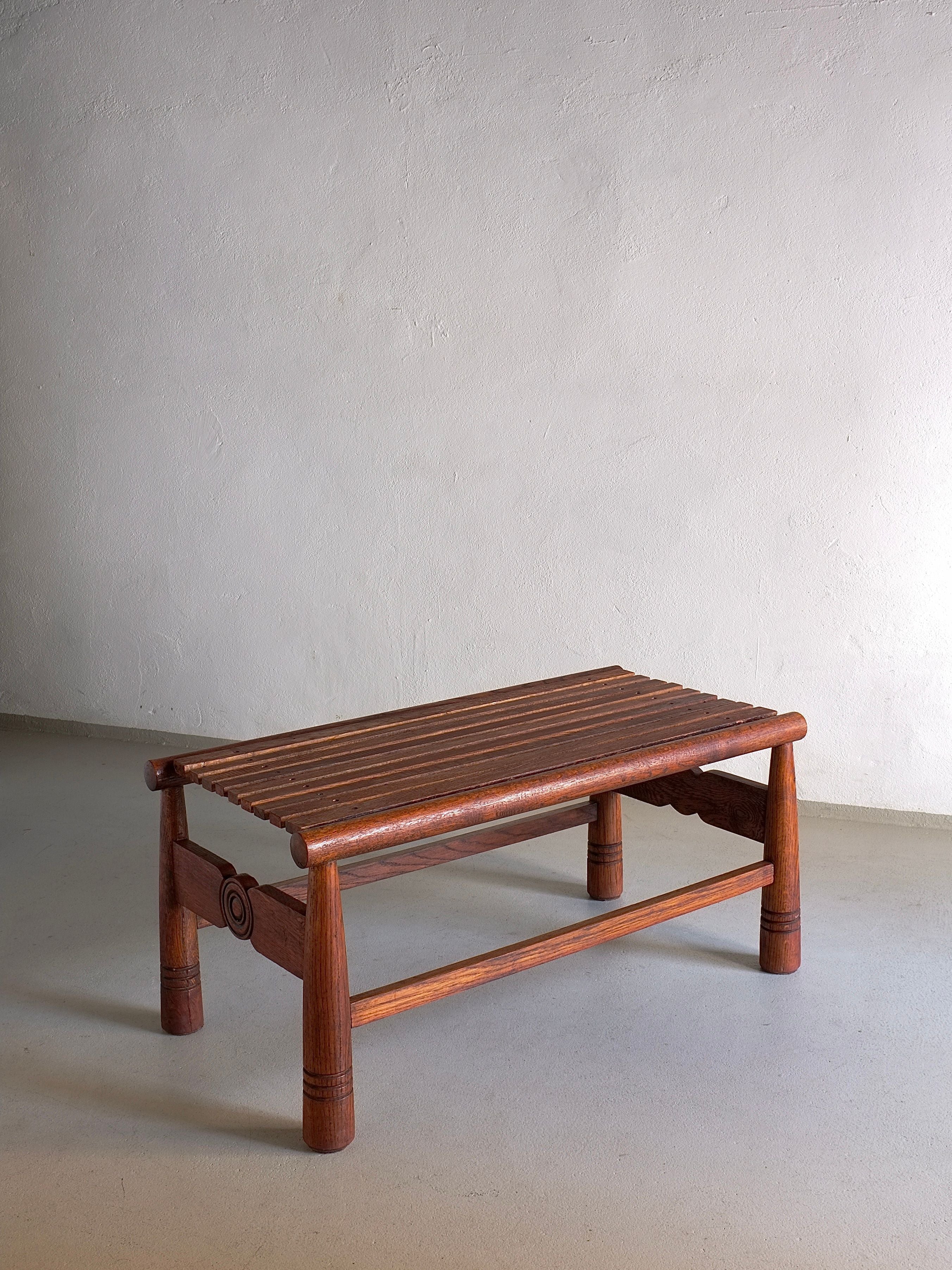 A Carved Dark Oak Bench from the 1960s by Veter Vintage stands on a grey floor against a plain, light-colored wall. This vintage bench from France boasts a slatted seat and decorative carved details on the legs. It has a simple yet rustic rectangular design and sturdy build, retaining its vintage condition.