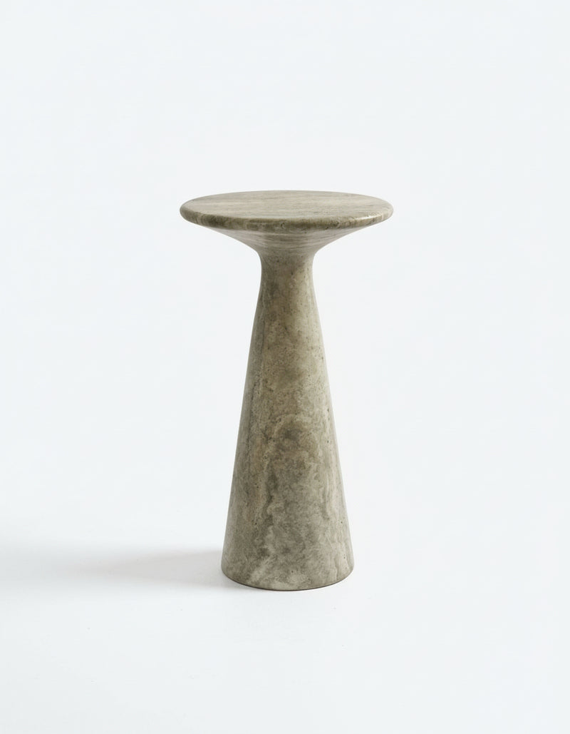 The Juno Tall Travertine Side Table by Ransom & Dunn is a minimalist stone pedestal table, handcrafted in Europe from silver travertine, showcasing a circular top and a narrow conical base against a plain white background.