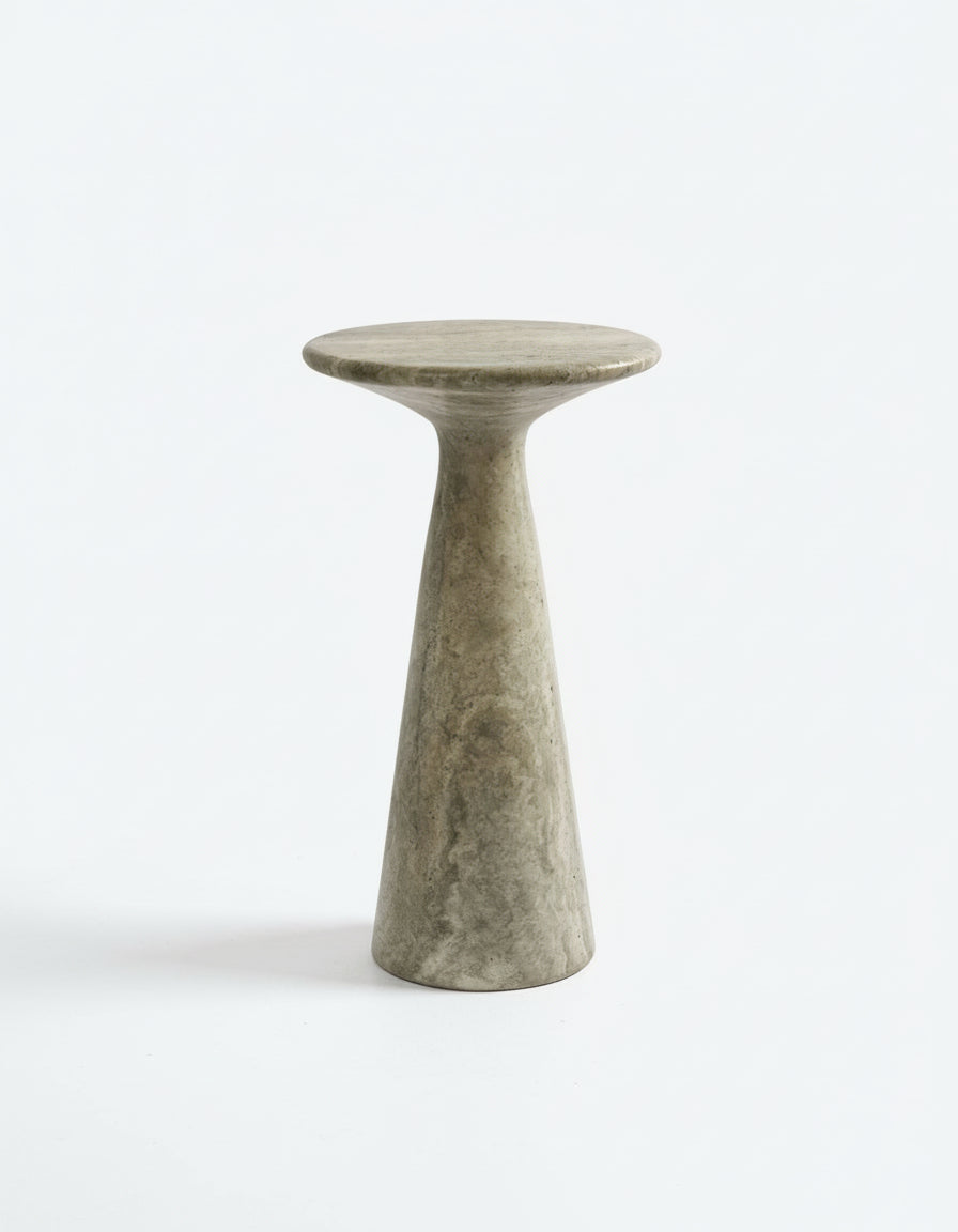 The Juno Tall Travertine Side Table by Ransom & Dunn is a minimalist stone pedestal table, handcrafted in Europe from silver travertine, showcasing a circular top and a narrow conical base against a plain white background.
