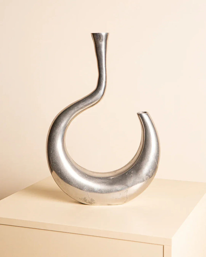 The Vase "Ondule" in Aluminum 80's by Treaptyque features a sleek, modern asymmetrical design, resting on a light surface against a beige backdrop, capturing the chic essence of Milan design.