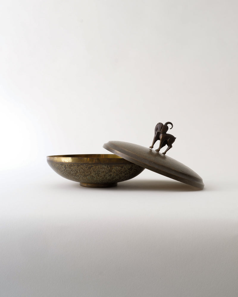 The Deco Box by Pierre Amédée Plasait from Collection apart is a decorative Art Deco brass box with an ornate lid, slightly open, topped with a small animal figurine as the handle. Set against a plain white background.