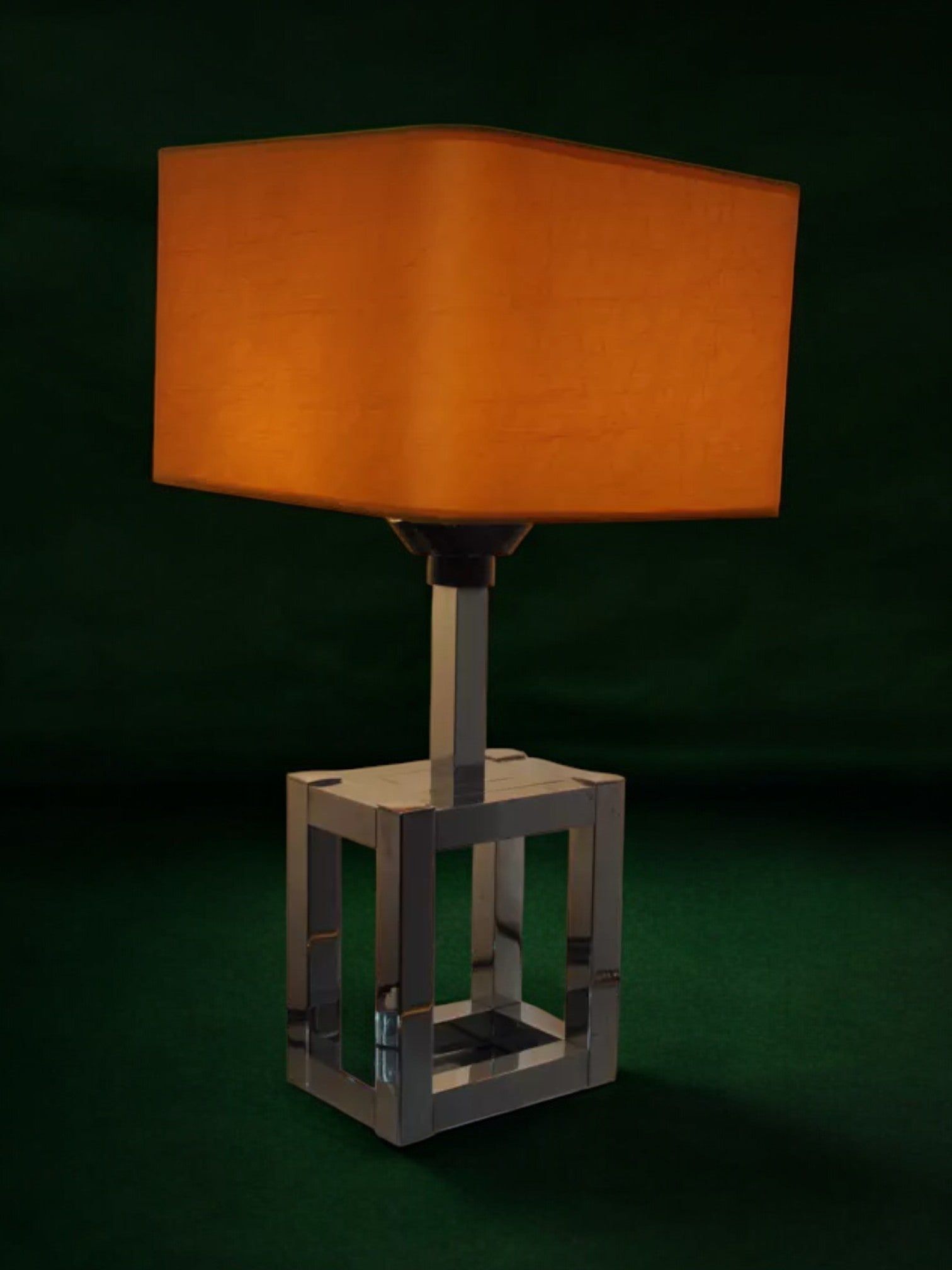 The BD Lumica Cubic Table Lamp by Malamar Studio, Italy 1970, features an orange rectangular shade and chromed cubic base—an iconic design objet for contemporary interiors, shown against a dark green background.