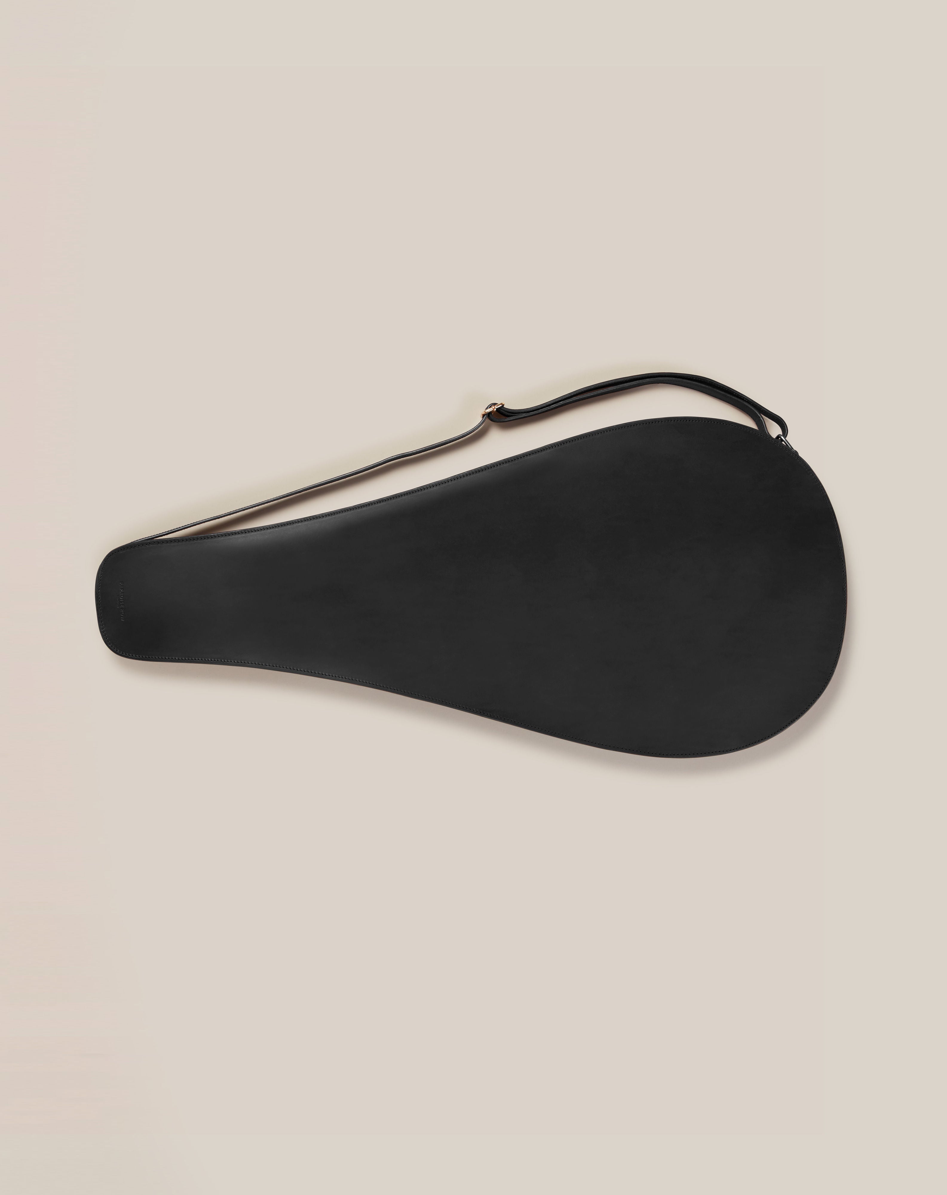 The Leather Tennis Racket Cover by Paradise Row showcases a bespoke British design, elegantly cradling your racket in a black teardrop shape. Made from sustainable vegetable-tanned leather with a convenient strap, it stands out on a plain light background, embodying style and sustainability.