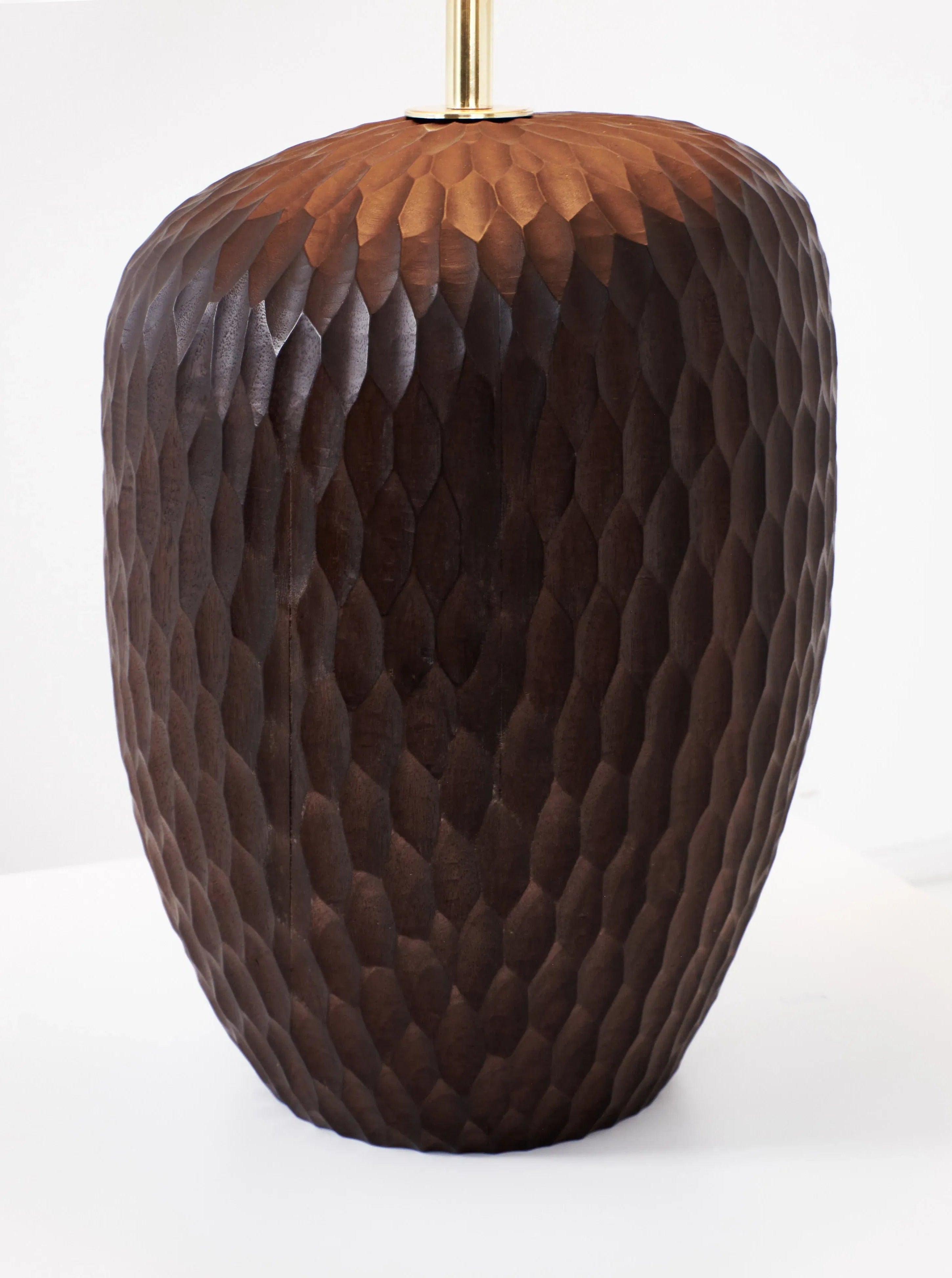 A close-up image of the Large Foz Lamp by Project 213A featuring a tall, dark wooden lamp base with a textured, faceted pattern. The solid wood has a rich brown color, and the top part of a gold-colored lamp rod is visible at the top. The background is a plain white surface.
