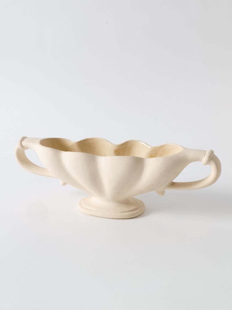 A cream-colored, ceramic serving dish with two symmetrical, ornate handles. The dish has a scalloped edge and a slightly elevated base, giving it an elegant, vintage appearance. Made from Devon clay by Collection apart, the background is plain white.