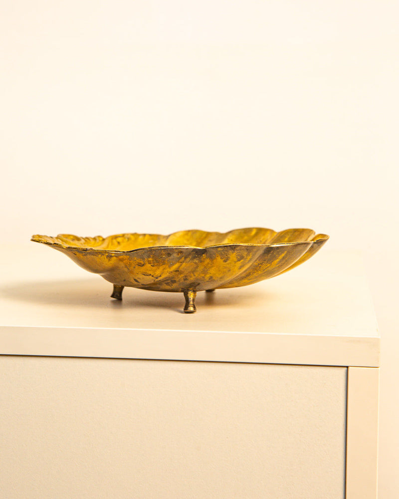 The Large Vide-poches Saint Jacques in Brass 60's by Treaptyque, featuring a gold scallop shell design and three small legs, sits atop a white cabinet set against a plain, light-colored background.