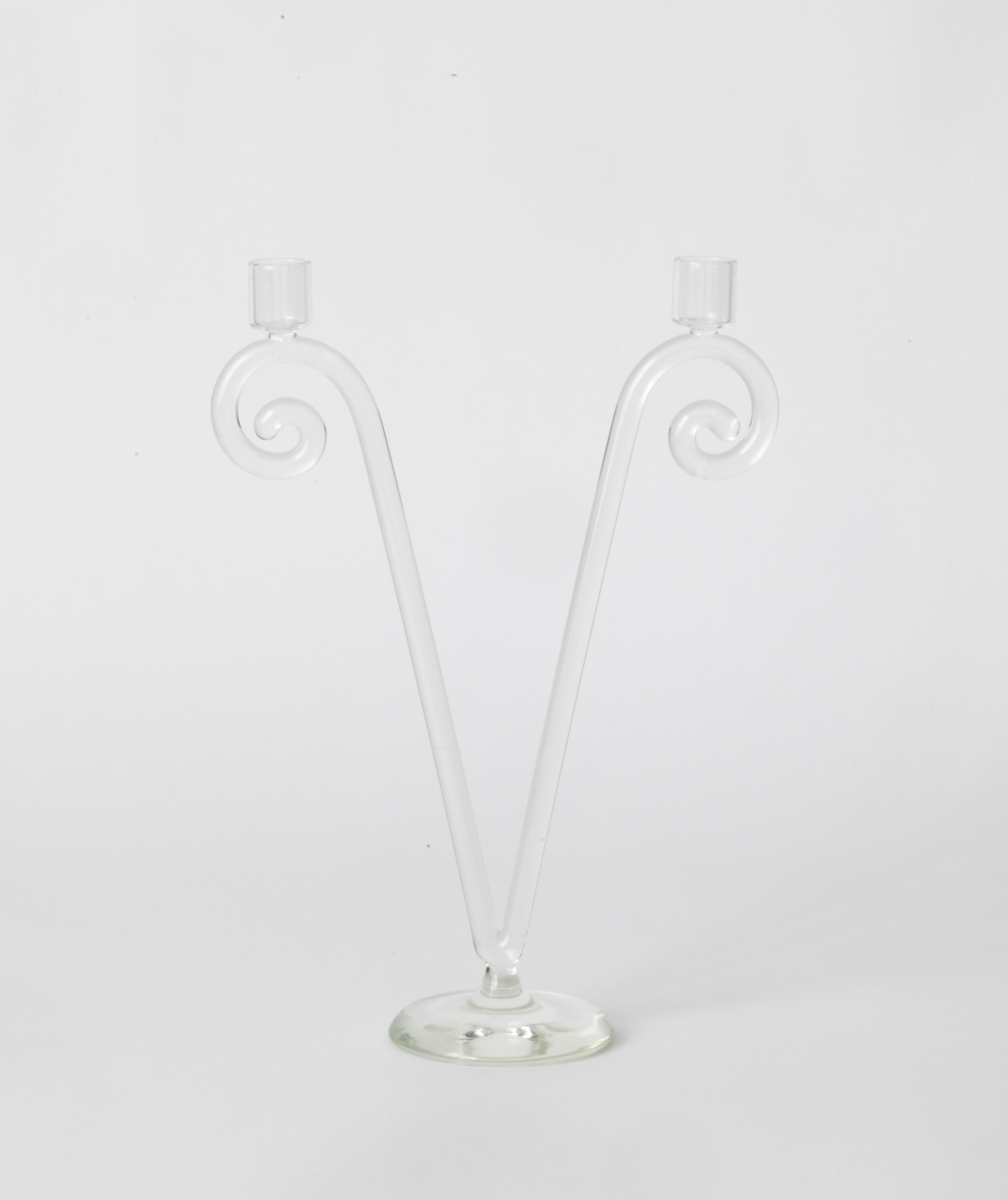 The Double Stem Spiral Candleholder by Sophie Lou Jacobsen features two upward-curving arms forming a wide "V," each with a candle holder. This clear glass piece stands on a round base, adding old-world charm to any dining setting.