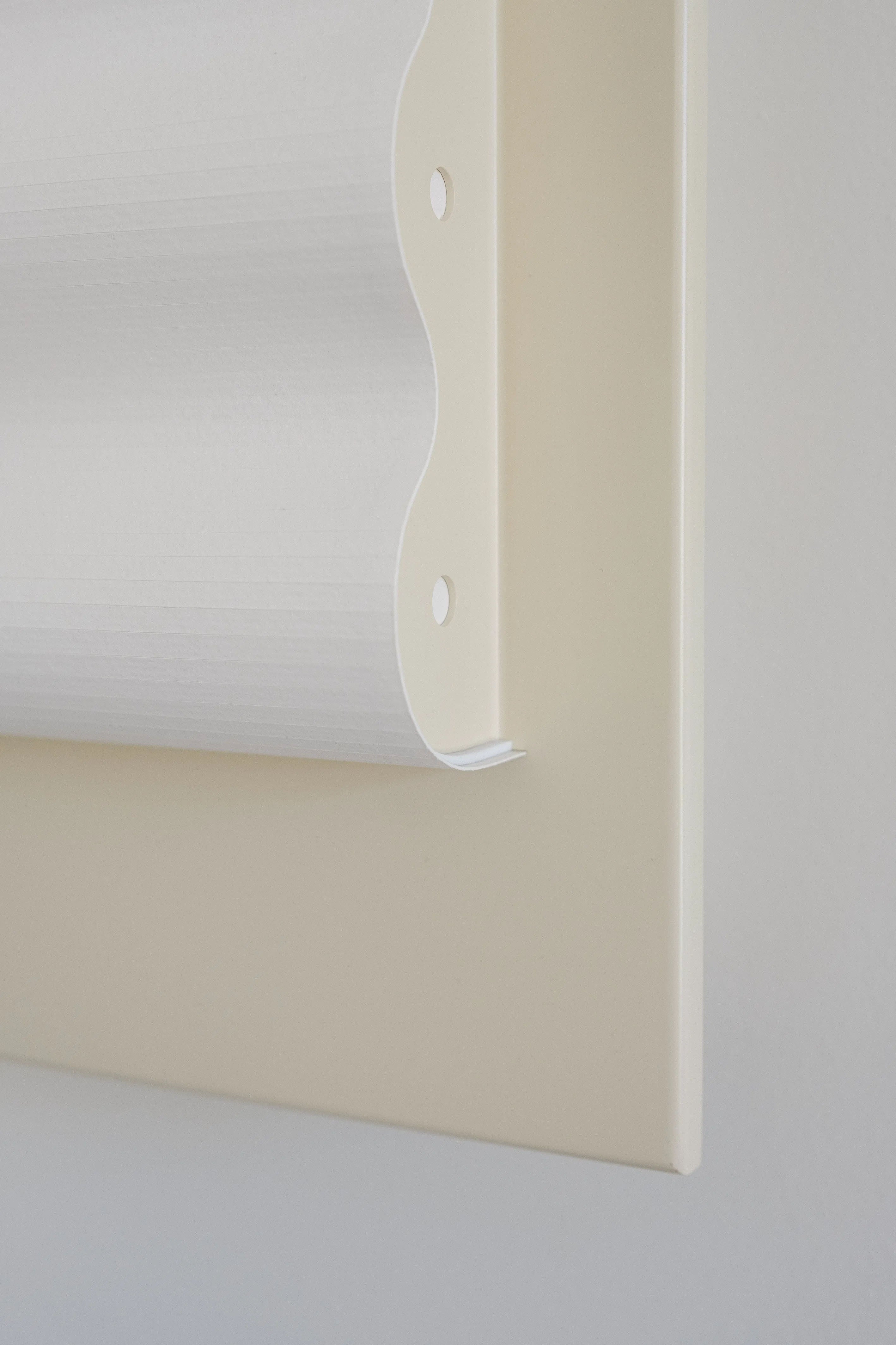 A close-up of the Violaine d'Harcourt Wall Light Frame OW S on a cream wall shows its minimalist design with a handcrafted scalloped edge and attachment hole, perfectly complementing any decor.