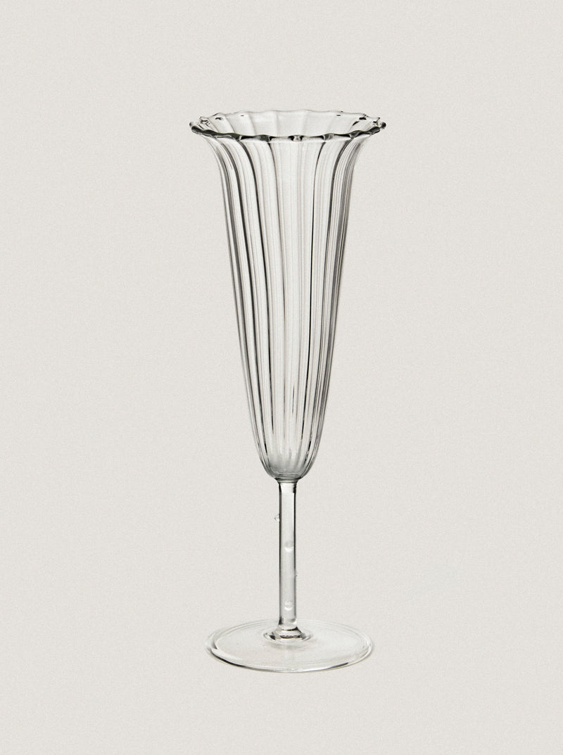 A clear, intricately designed Sophie Lou Jacobsen Angel Flute - Set of Four stands on a flat base. The vases feature vertical ribbed lines running from top to bottom, with scalloped, flared rims accentuating their elegant forms. Imagine them each holding an Angel Trumpet flower against the simple, light beige background.