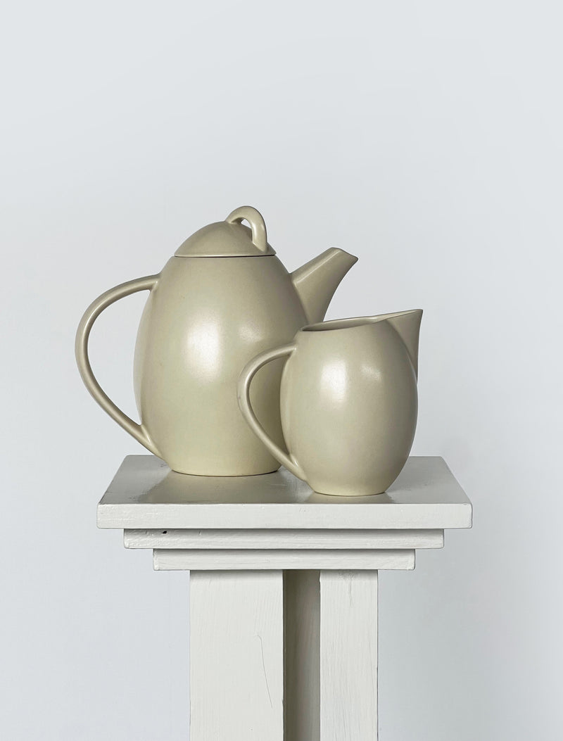 Sage green ceramic teapot and milk jug set on white pedestal
