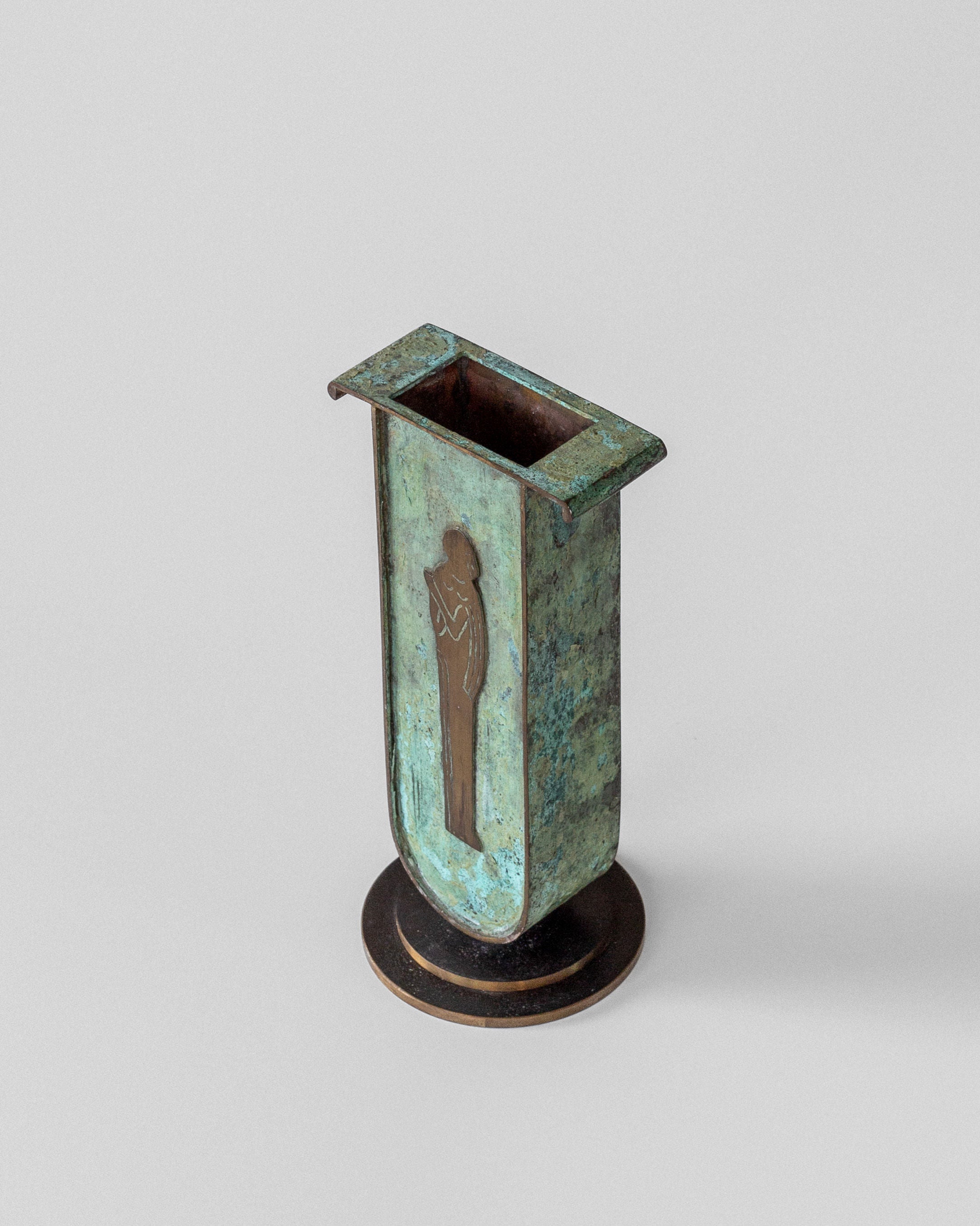 The Spigel Art Deco Brass Vase with Verdigris Patina is rectangular and features a silhouette of a person playing a horn. It rests gracefully on a round base, reminiscent of Swedish design.