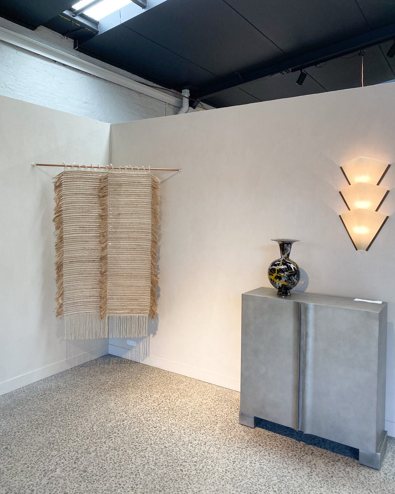 Gallery corner displaying woven textile sculpture and ceramic vase