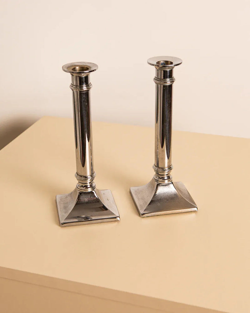 A pair of metal Candleholders "Colonne" 80's from Treaptyque are positioned side by side on a light-colored surface against a neutral background. These Italian candleholders feature a classic and sleek design with subtle vintage industrial touches.
