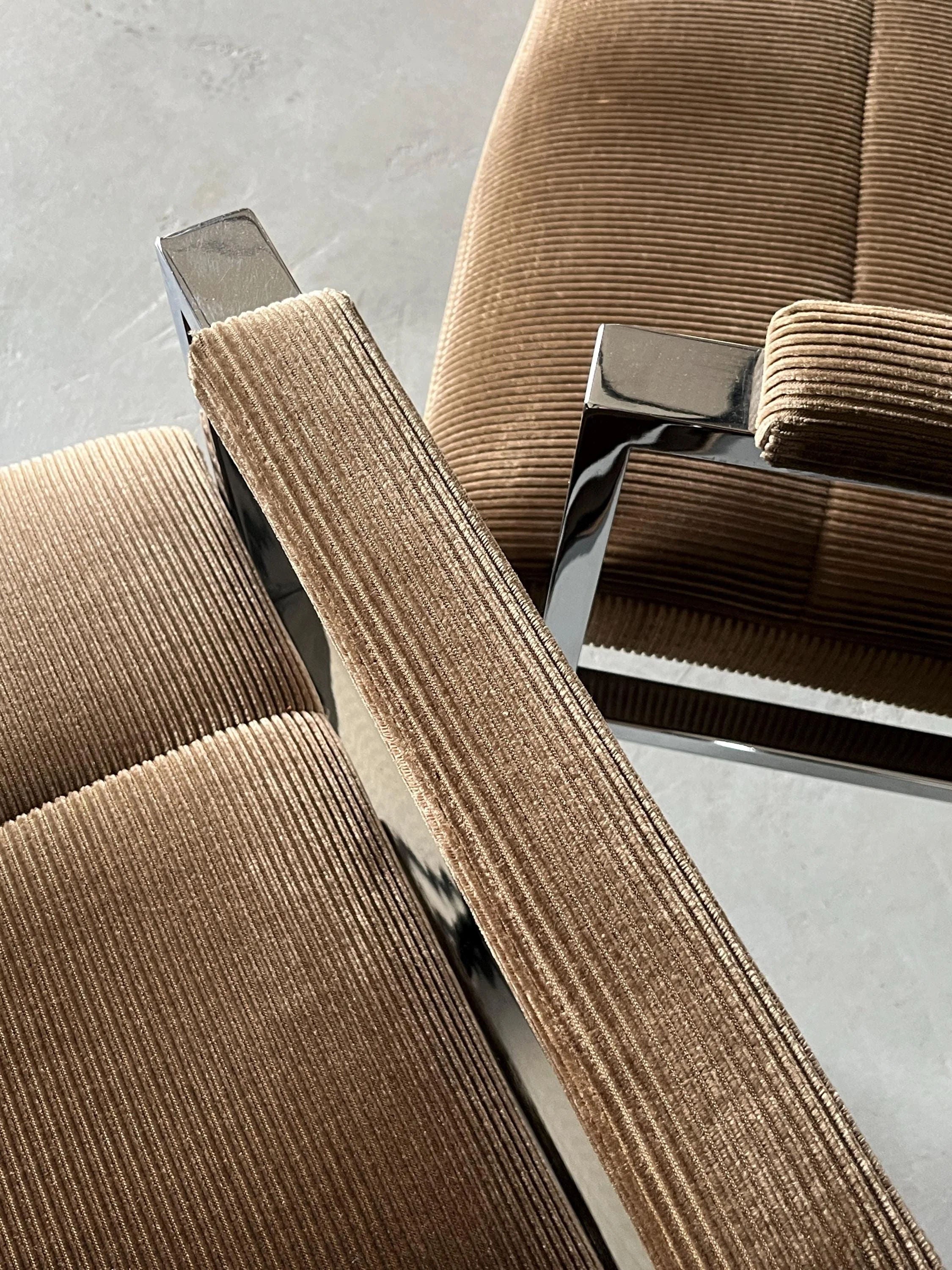 Close-up of two Cherry Cargo Mid-Century Armchairs, 1970s, showcasing brown corduroy upholstery and chrome steel frames on a light gray floor. The fabric texture and sleek metallic finish are prominently visible.