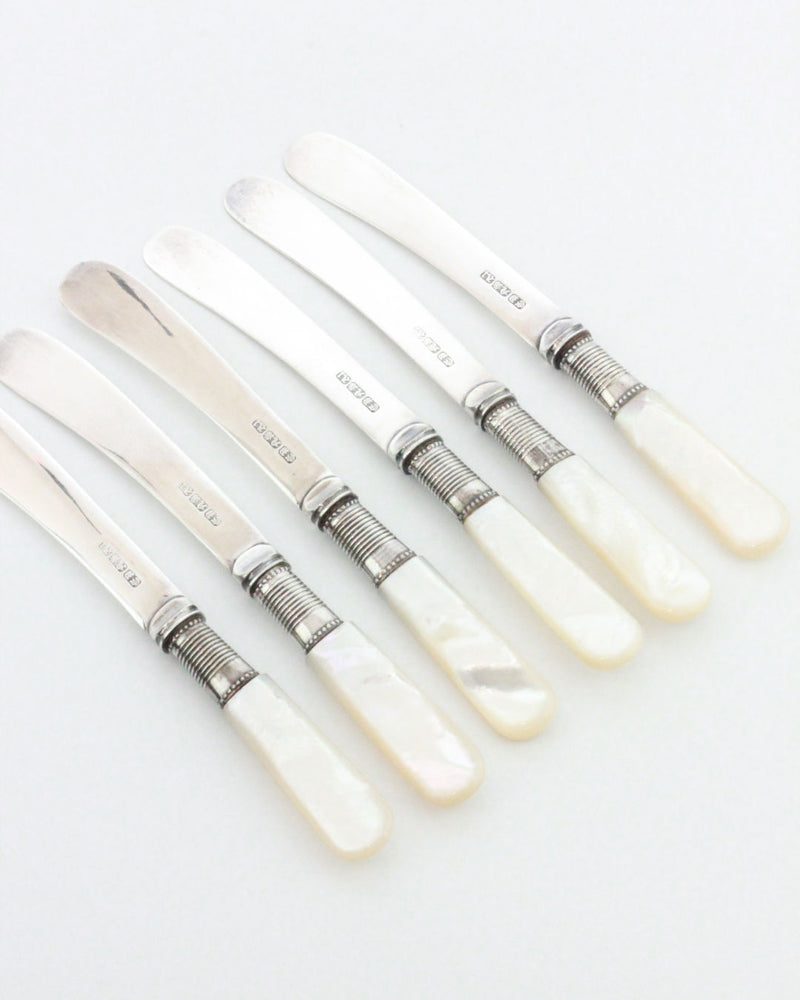A set of six Boga Avante Shop Mother-of-pearl Butter Knives with shiny metal blades and smooth white mother-of-pearl handles displays classic vintage style, arranged diagonally on a plain white background.