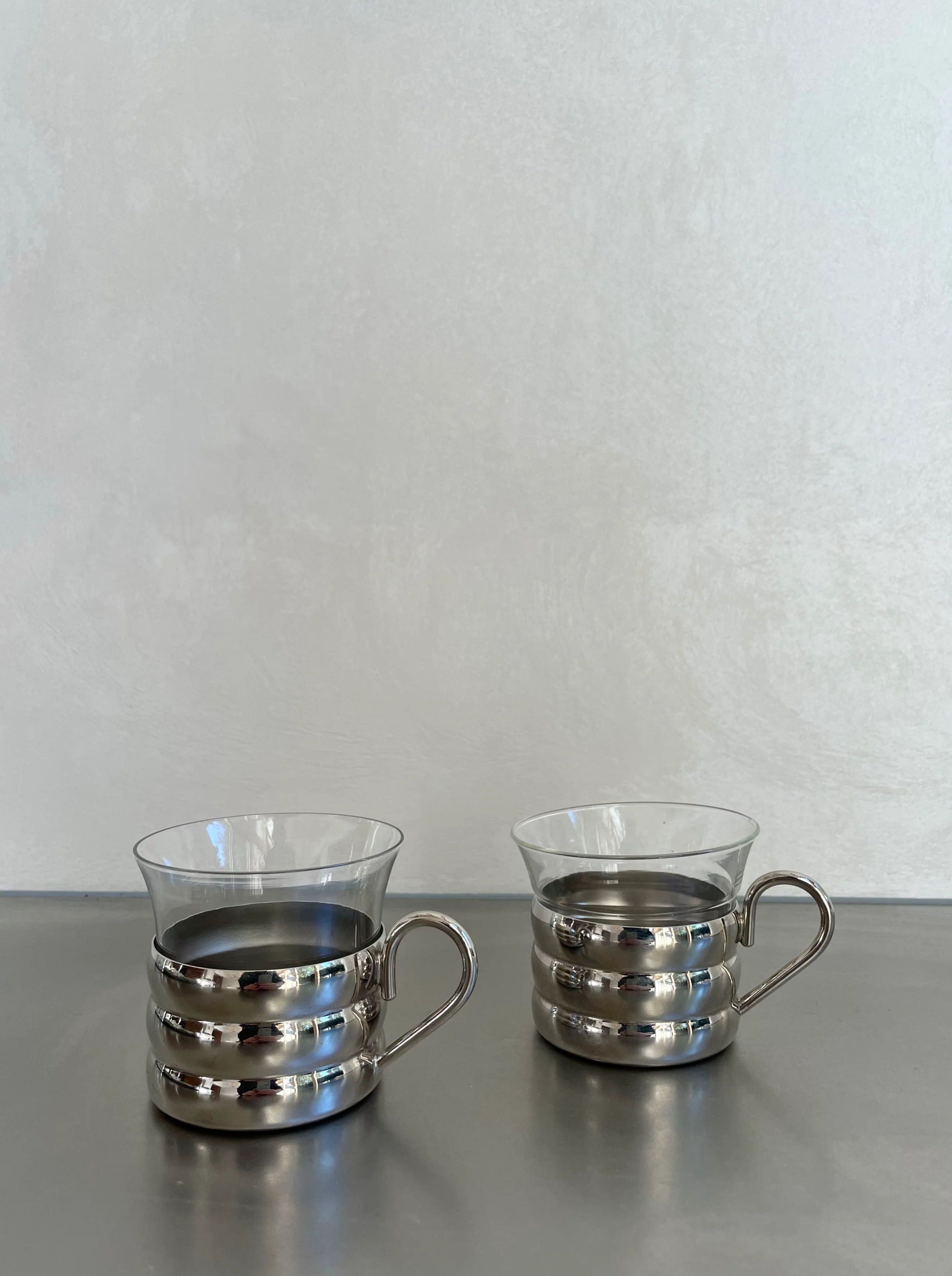 A set of six glass cups with a sleek stainless steel holder