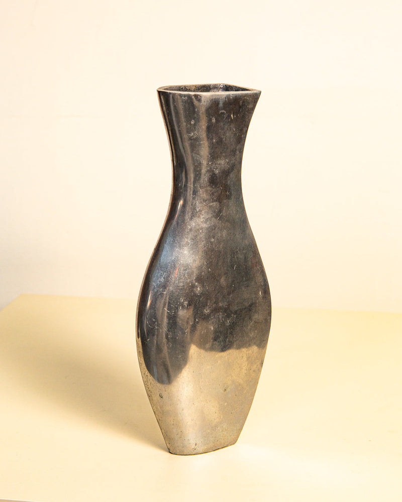 The Italian Vase "Dame" by Treaptyque from the 80's is a tall, sleek cast aluminum piece with a narrow neck and wide base. It features a reflective surface and stands on a light-colored surface against a neutral background, epitomizing minimalist design.