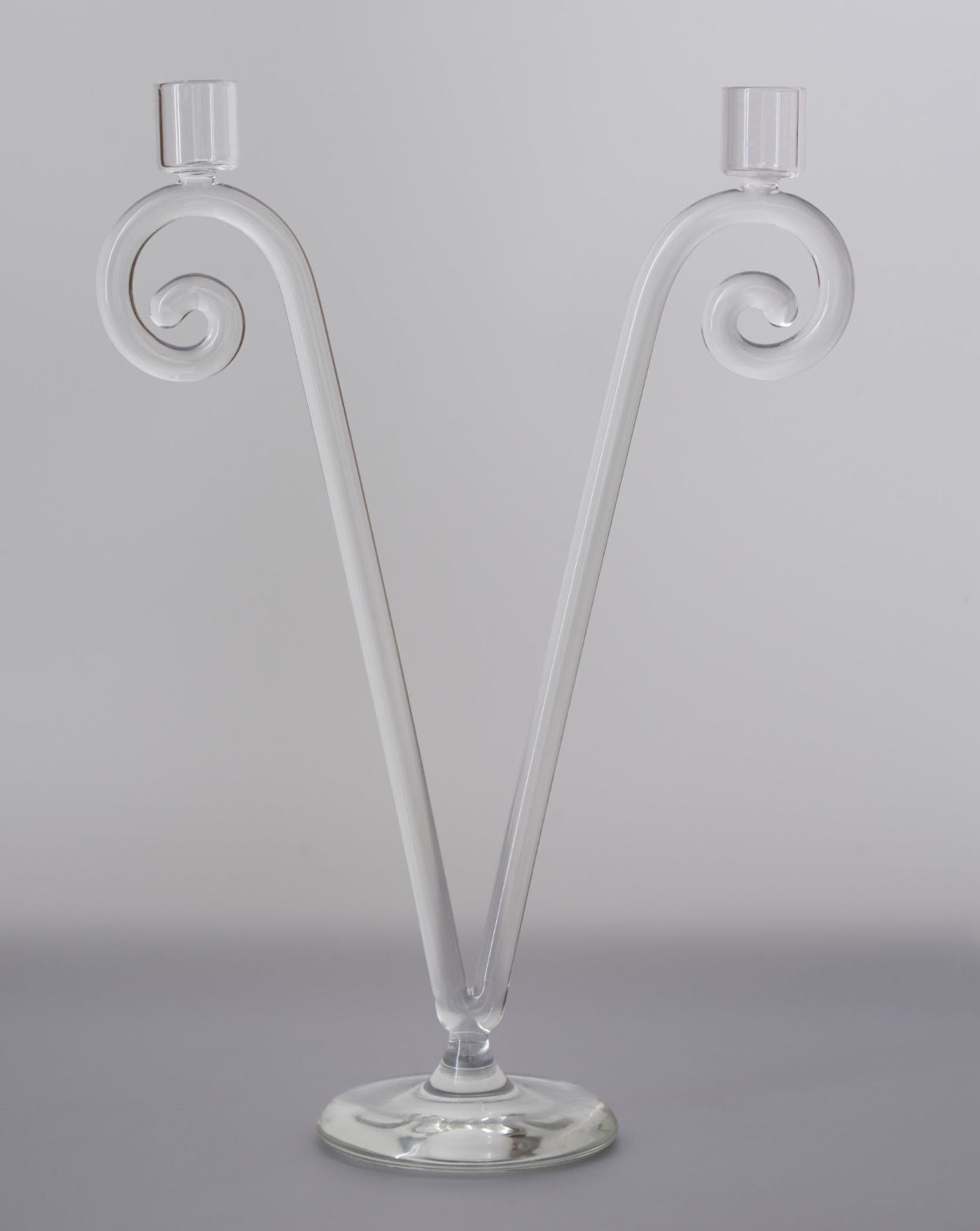 The Double Stem Spiral Candleholder by Sophie Lou Jacobsen features two clear glass arms curving in a V-shape with candle cups on a round base—an elegant accent for classic dining or decorative art lovers.