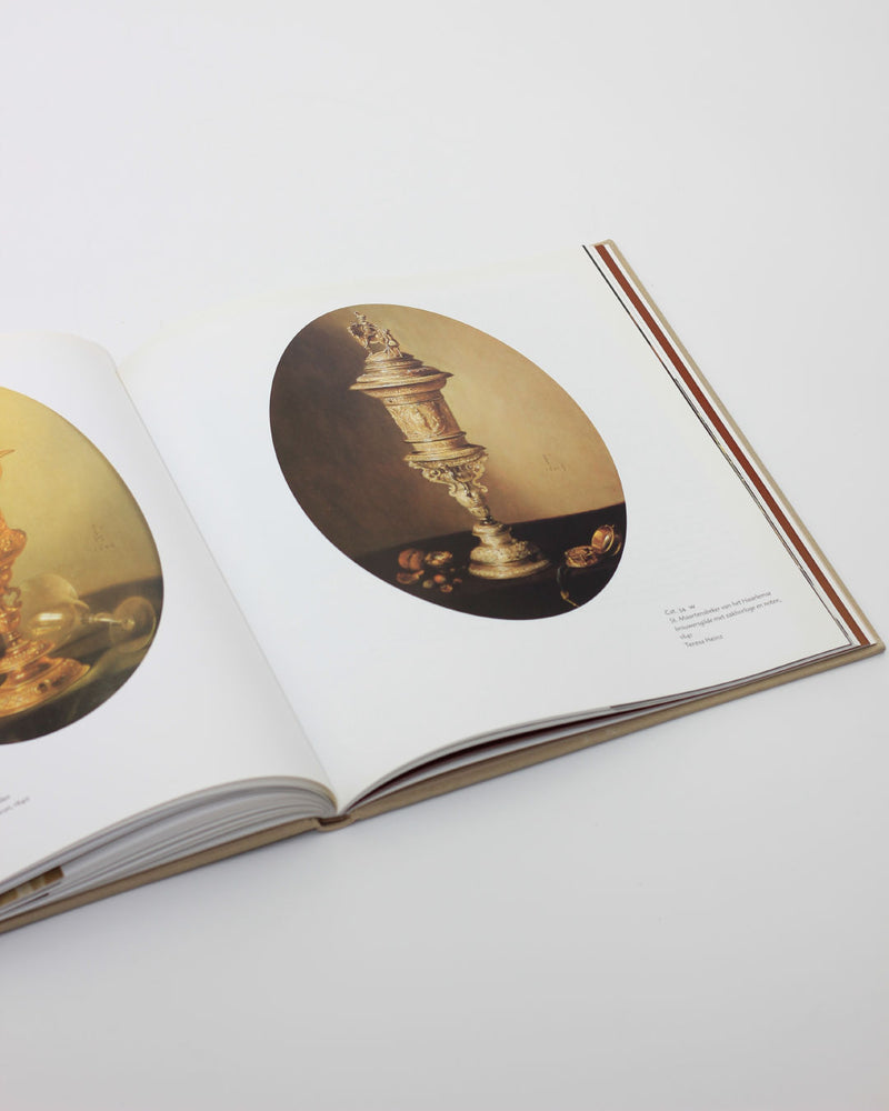 Open Pieter Claesz art book showing ornate golden vessels detail